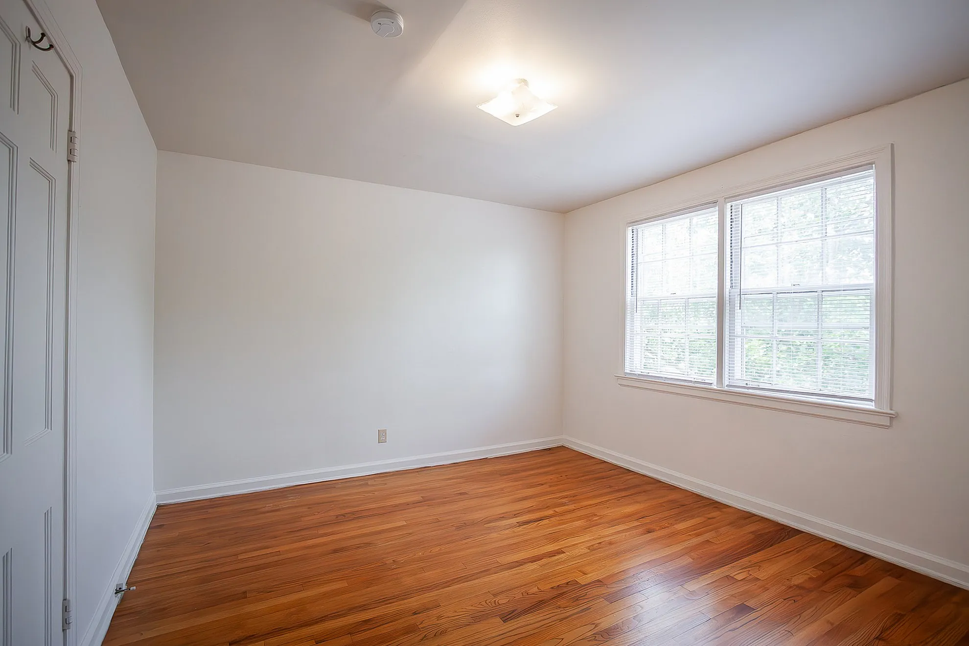 Bright and airy room with elegant hardwood flooring and large windows infusing natural light for a serene living space.