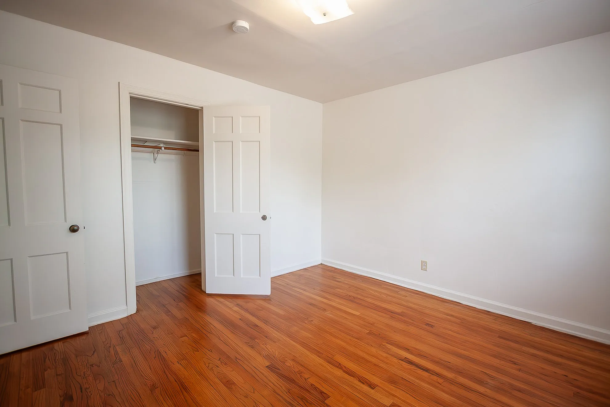 Bright and inviting bedroom with warm hardwood floors and spacious closet, perfect for customization.