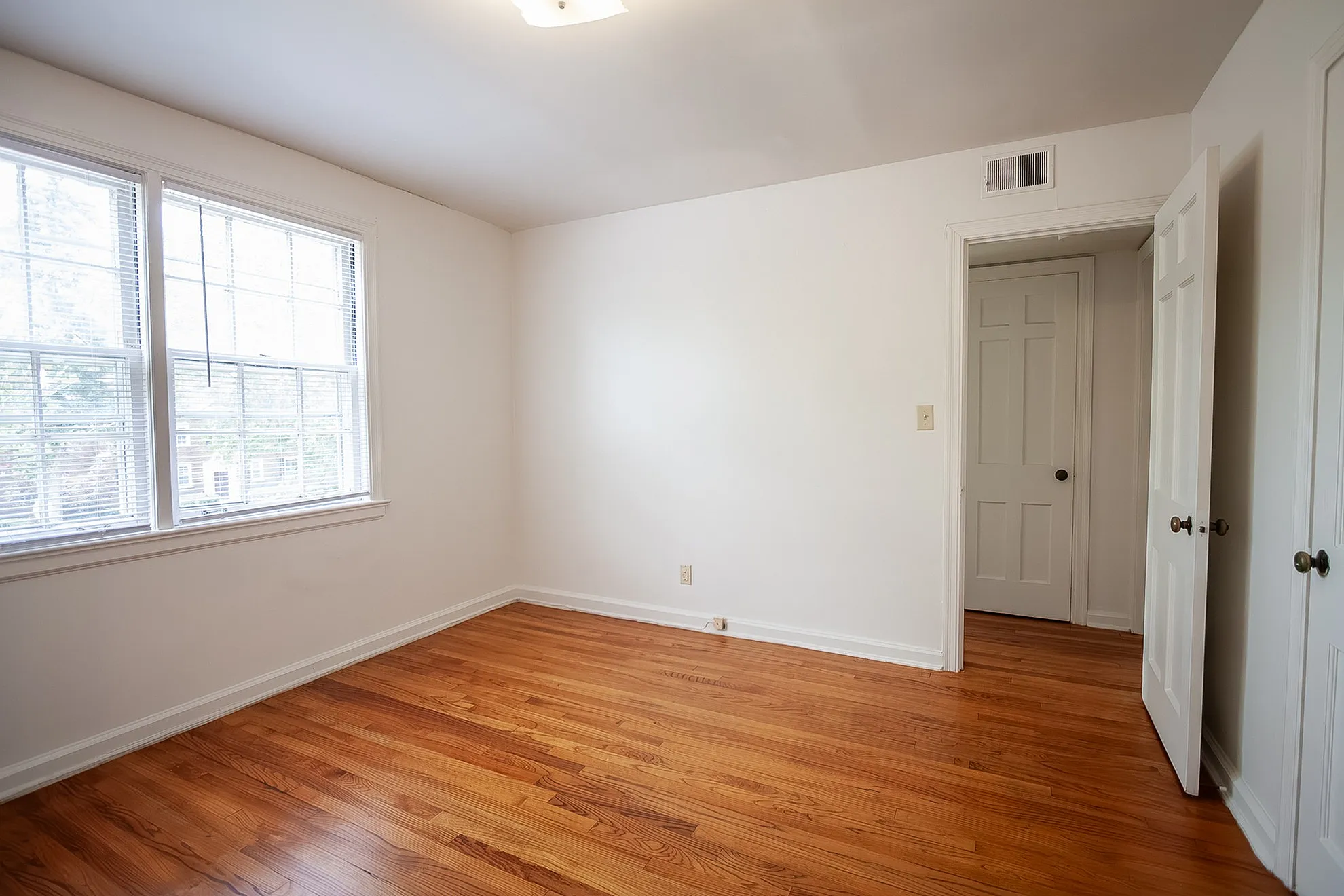 Bright, inviting bedroom with gleaming hardwood floors, fresh white walls, and abundant natural light from large windows.