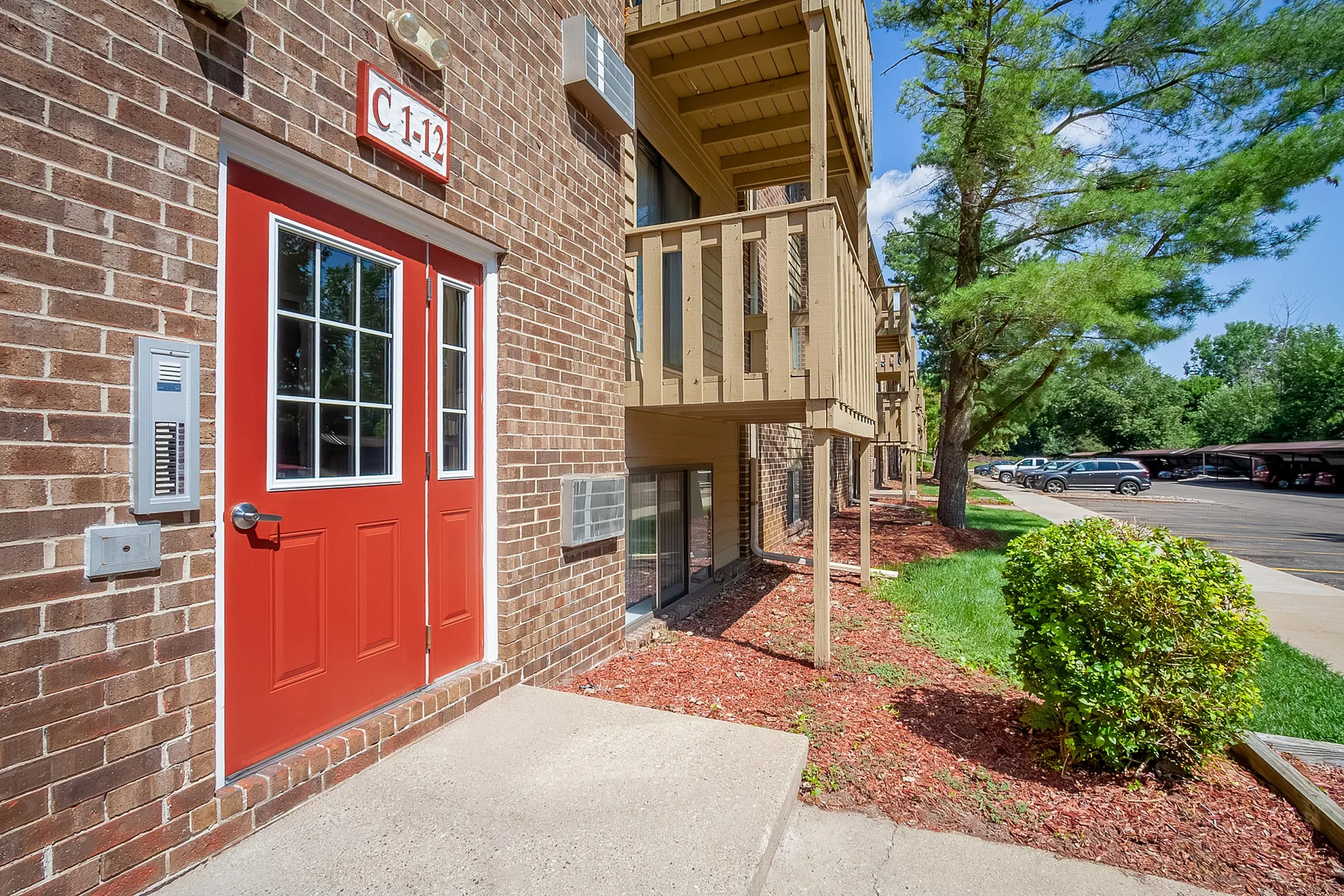 Charming apartment exterior with vibrant red door, private balconies, and a beautifully landscaped walkway.