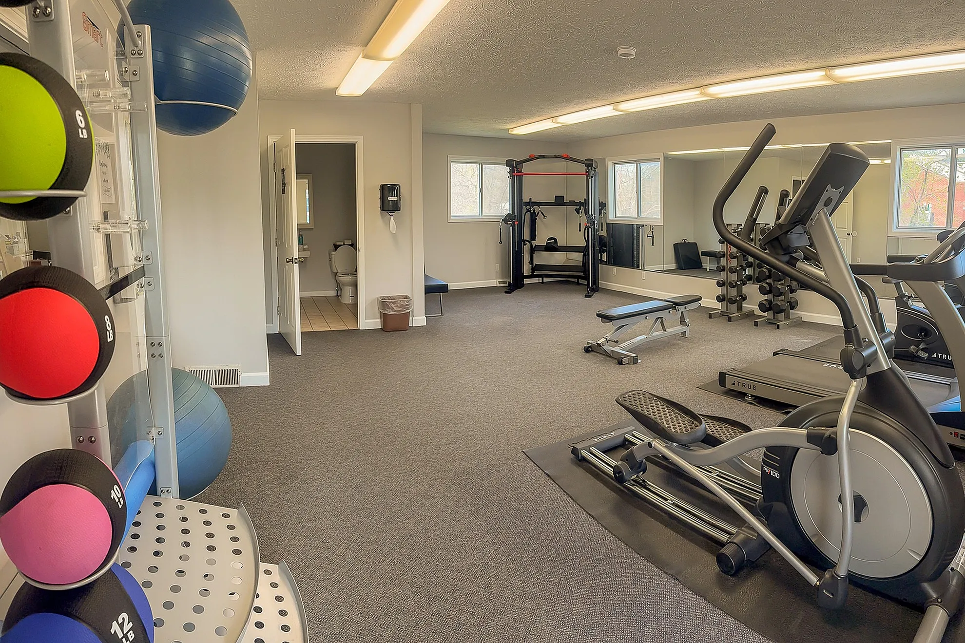 Modern fitness center with cardio machines, weights, and exercise balls, featuring bright lighting and spacious layout.
