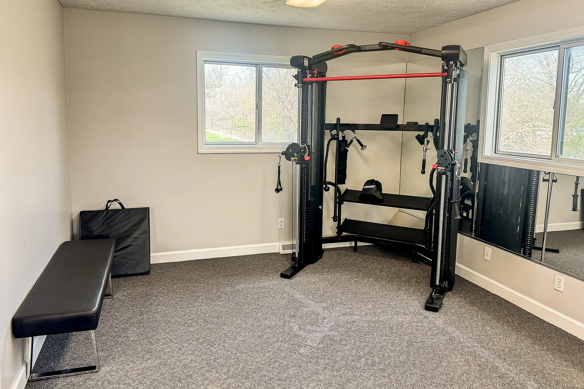 Bright and modern home gym featuring a multifunctional exercise machine and comfortable bench, with large windows providing ample natural light.
