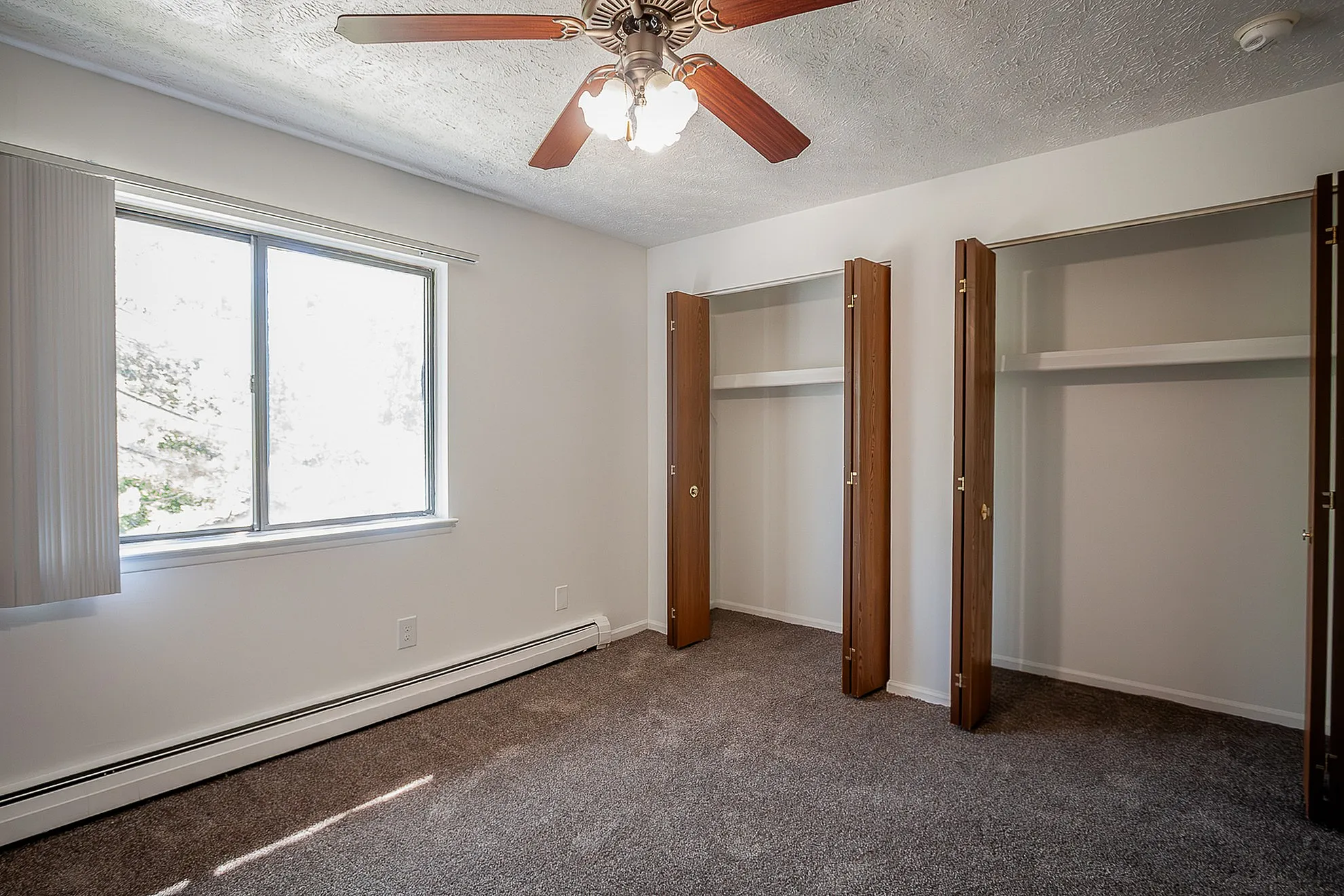 Bright bedroom with modern ceiling fan, dual closets, and large window offering abundant natural light.