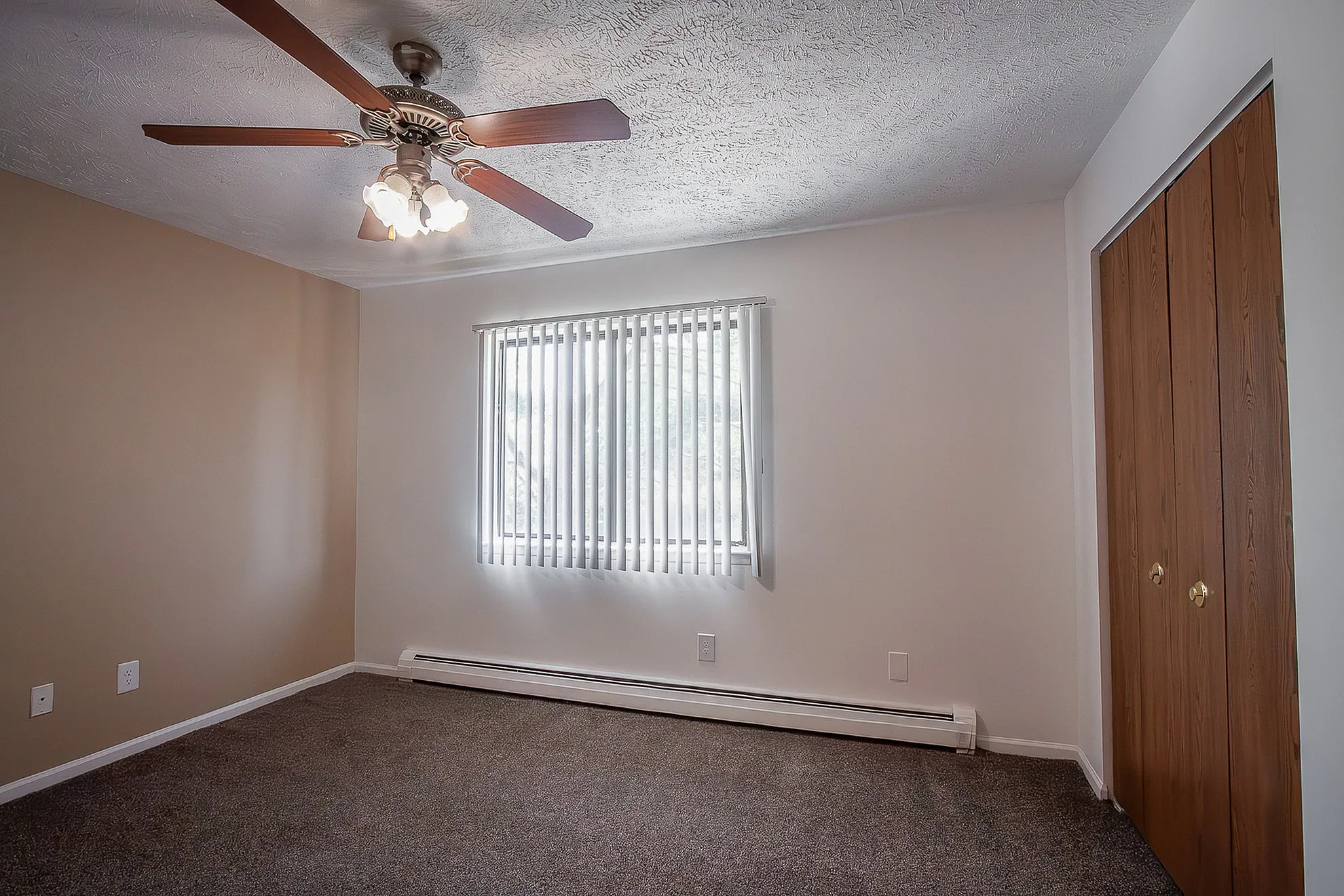 Inviting bedroom with warm tones featuring a stylish ceiling fan, textured ceiling, and large window with blinds offering ample natural light.