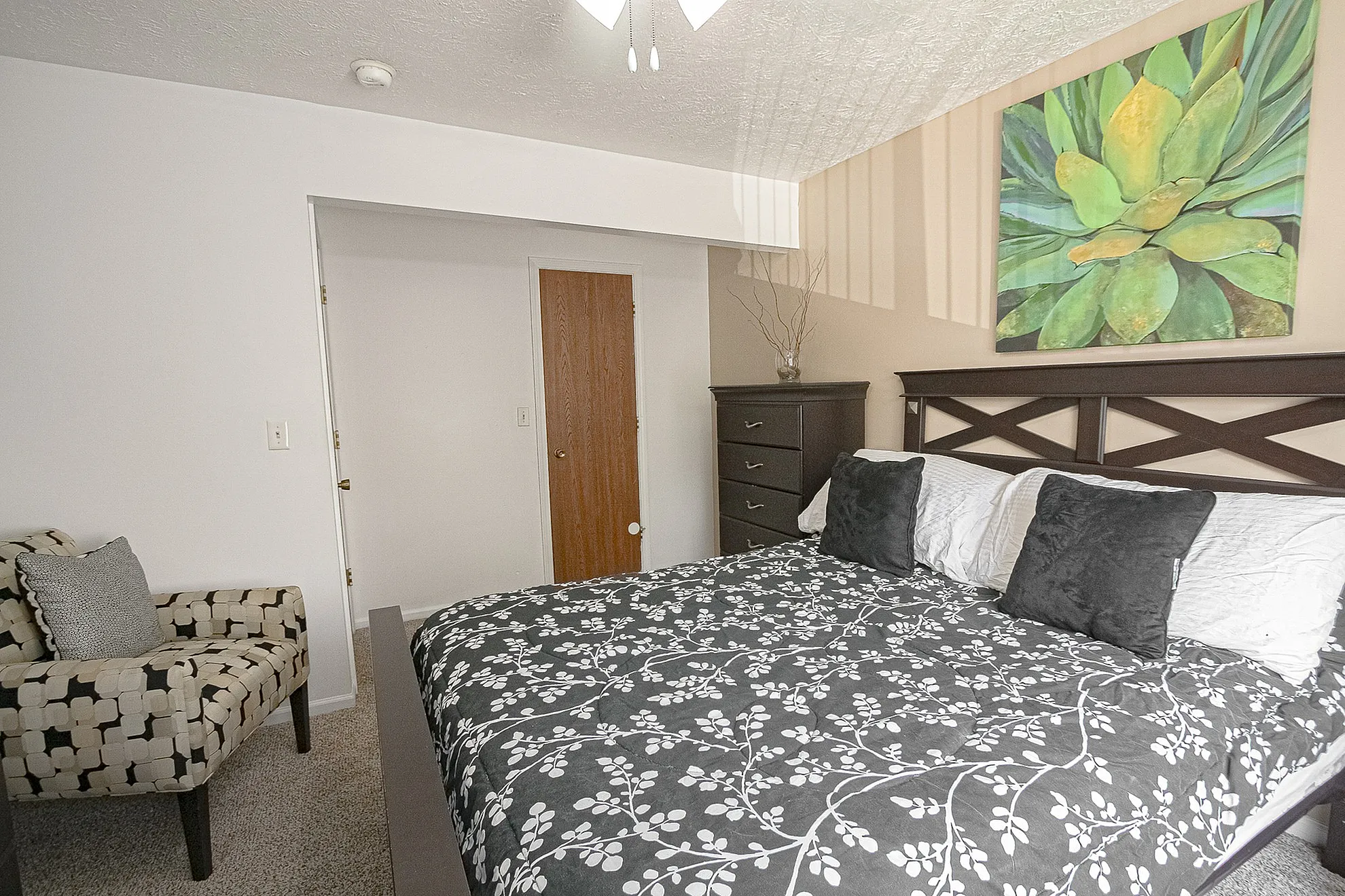 Inviting bedroom with a patterned comforter, elegant artwork, and cozy seating corner. Warm, stylish decor for a restful retreat.