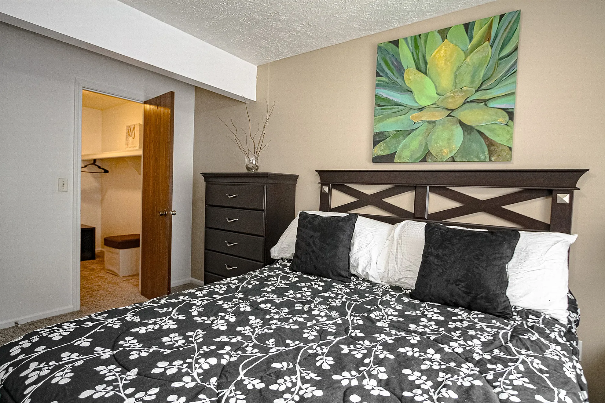 Inviting bedroom with a stylish dark wood headboard, vibrant plant artwork, and convenient walk-in closet access.