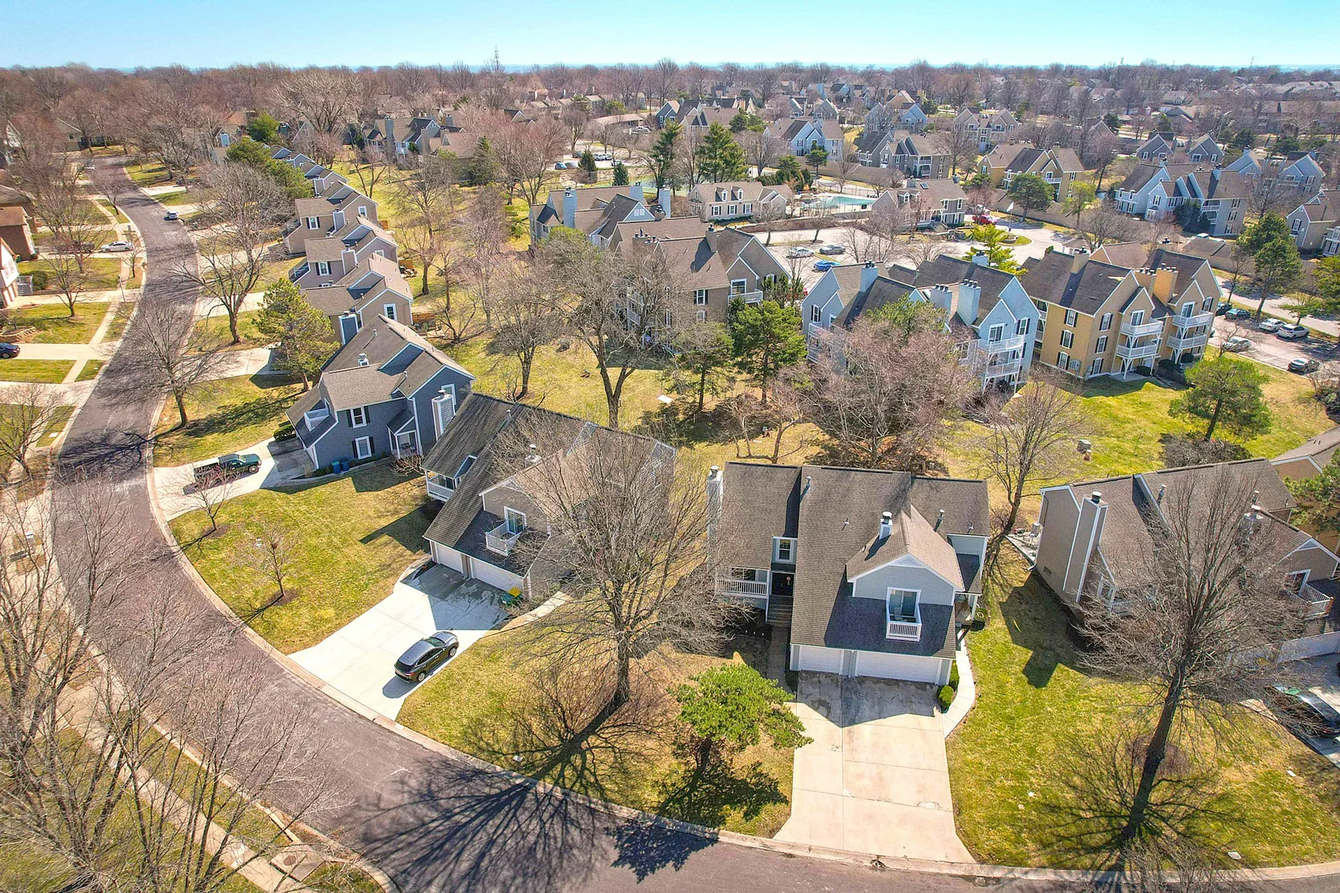 Charming aerial view of a picturesque suburban neighborhood with cozy homes, tree-lined streets, and lush greenery.