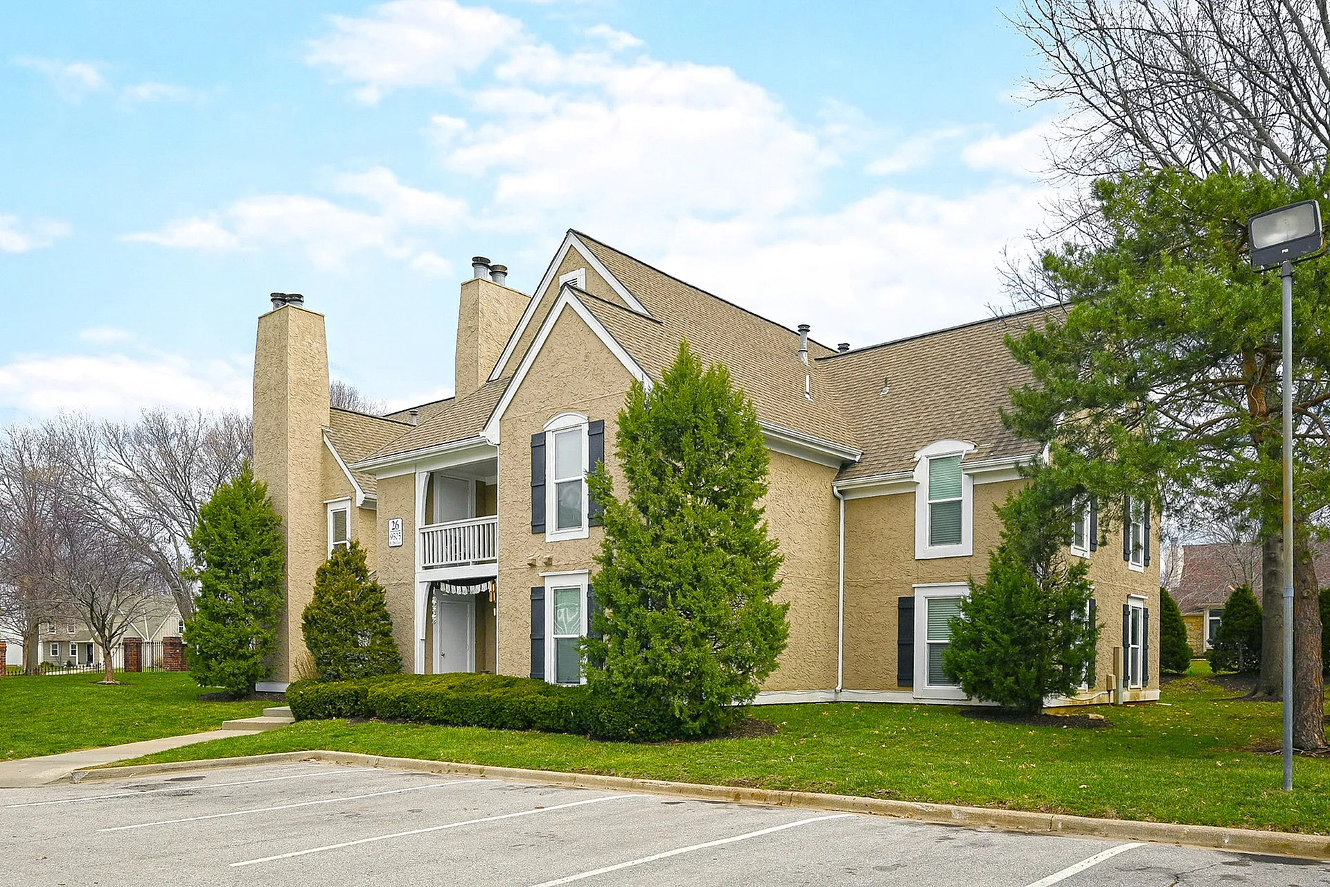 Charming two-story apartment building with modern design, surrounded by lush greenery and a spacious parking area.