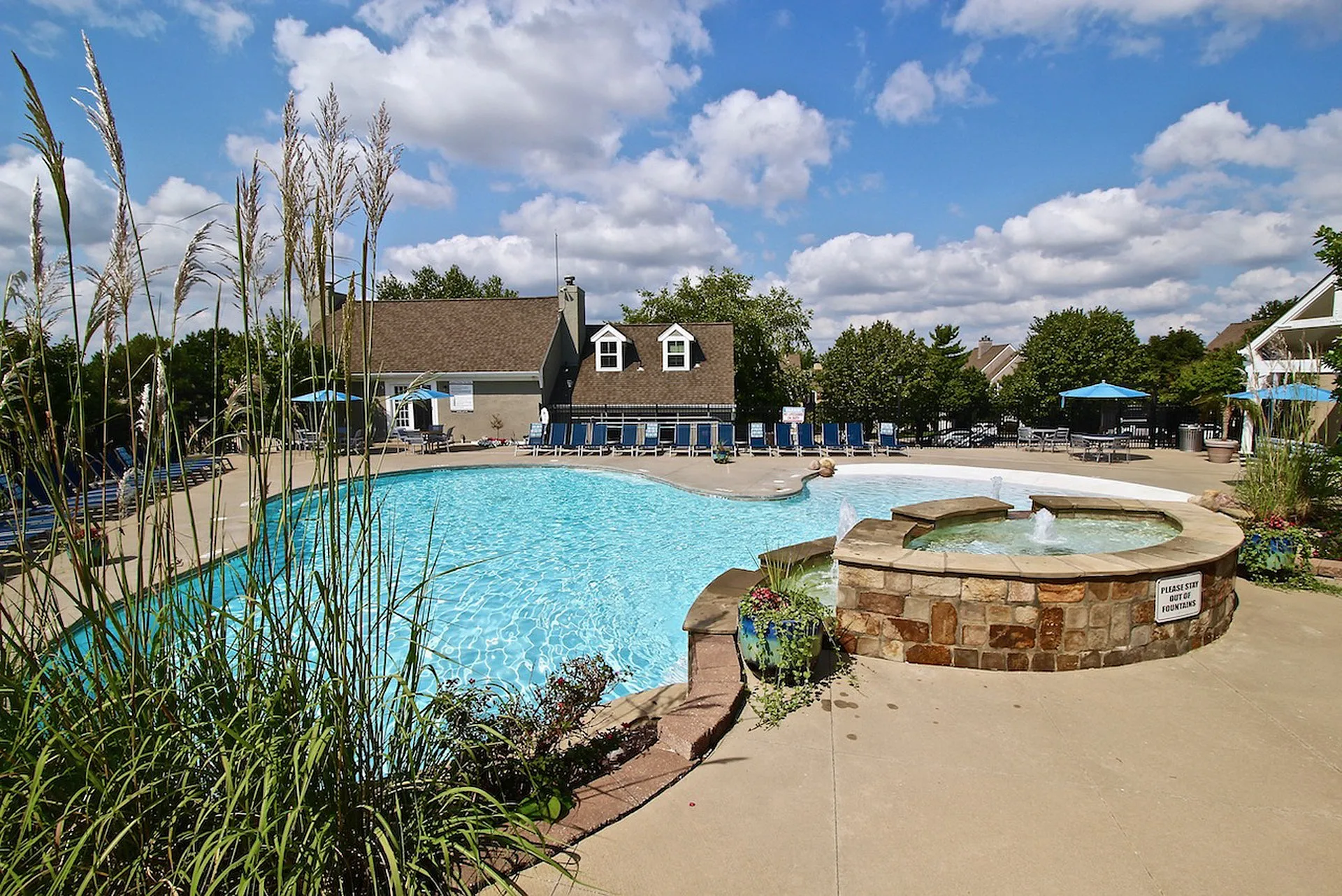 Inviting pool area with crystal-clear water, surrounded by lush greenery and cozy lounge chairs under vibrant blue skies.