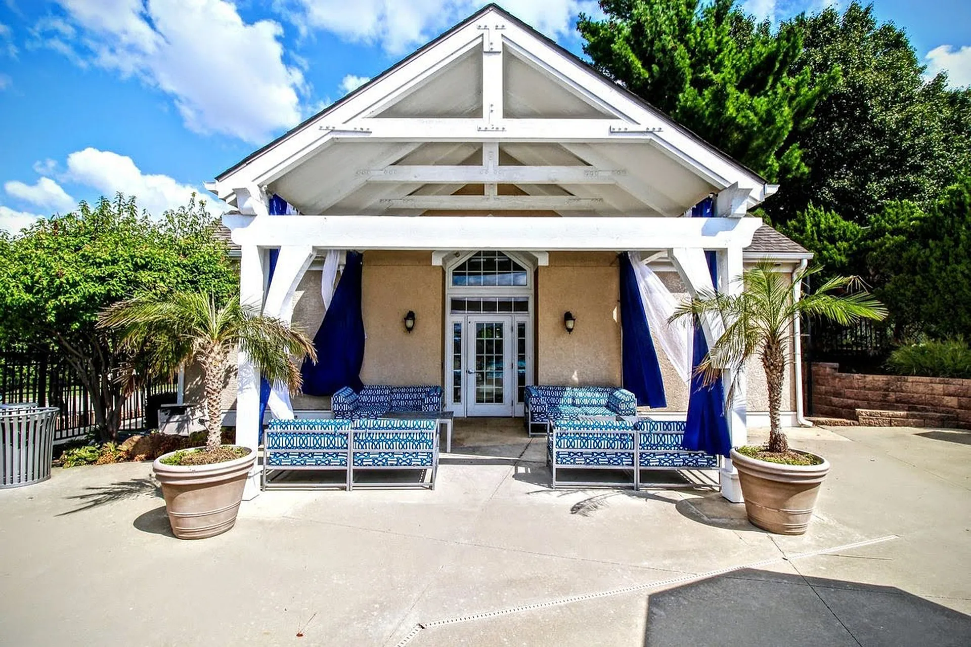 Elegant outdoor seating area featuring stylish blue and white cushions under a charming pavilion with tropical plants and vibrant greenery.