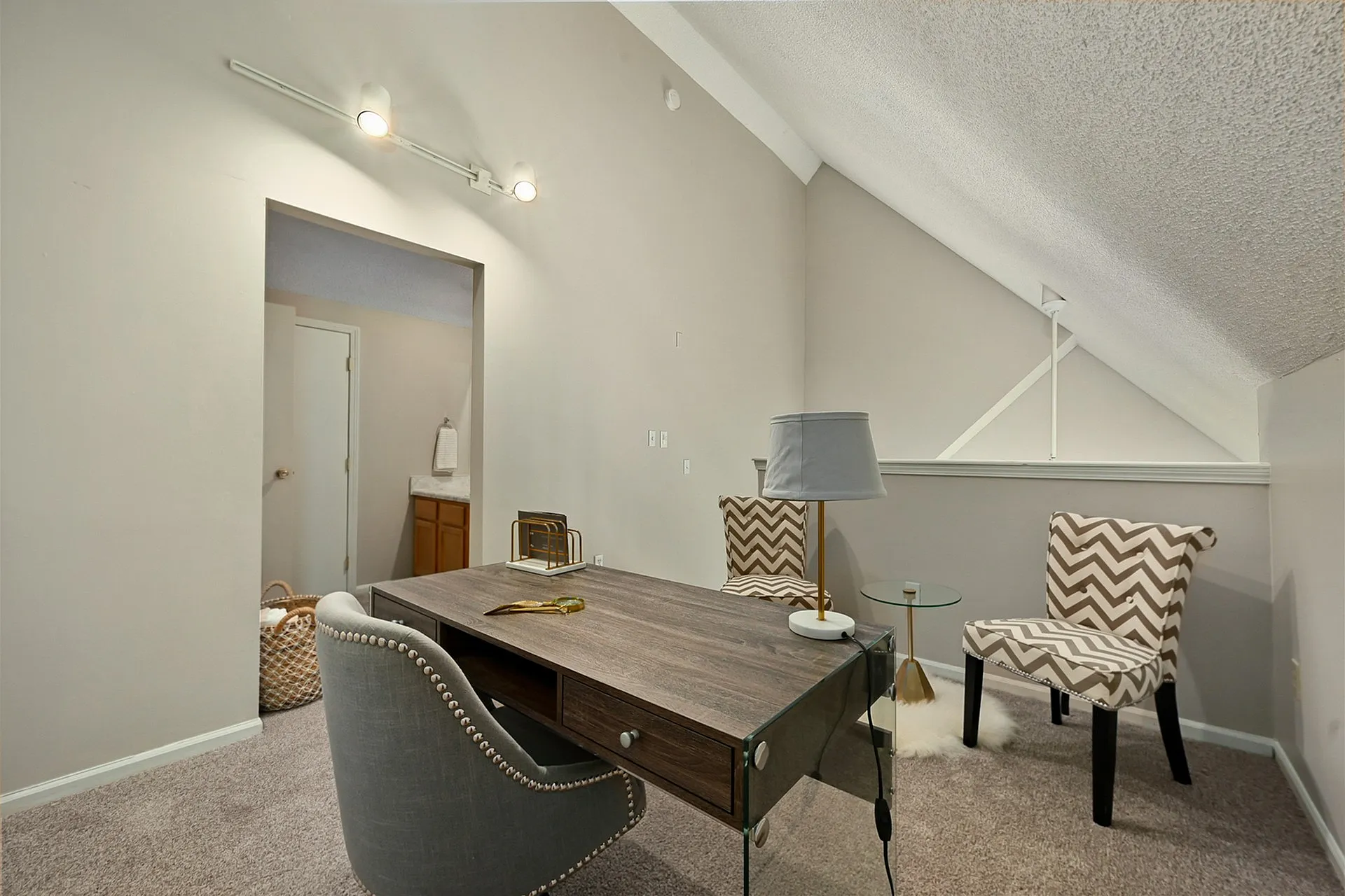 Chic home office with elegant glass-top desk, plush upholstered chair, and stylish zigzag pattern accents.