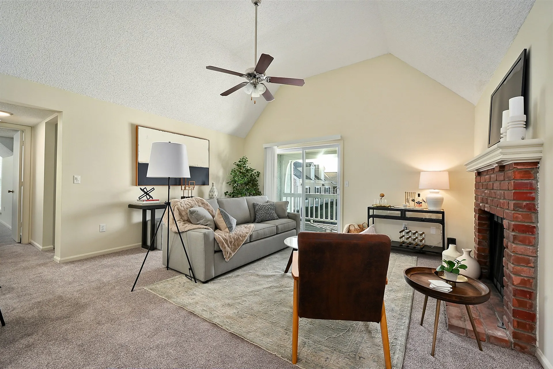 Cozy living room with vaulted ceiling, red brick fireplace, and stylish decor leading to a bright balcony view.