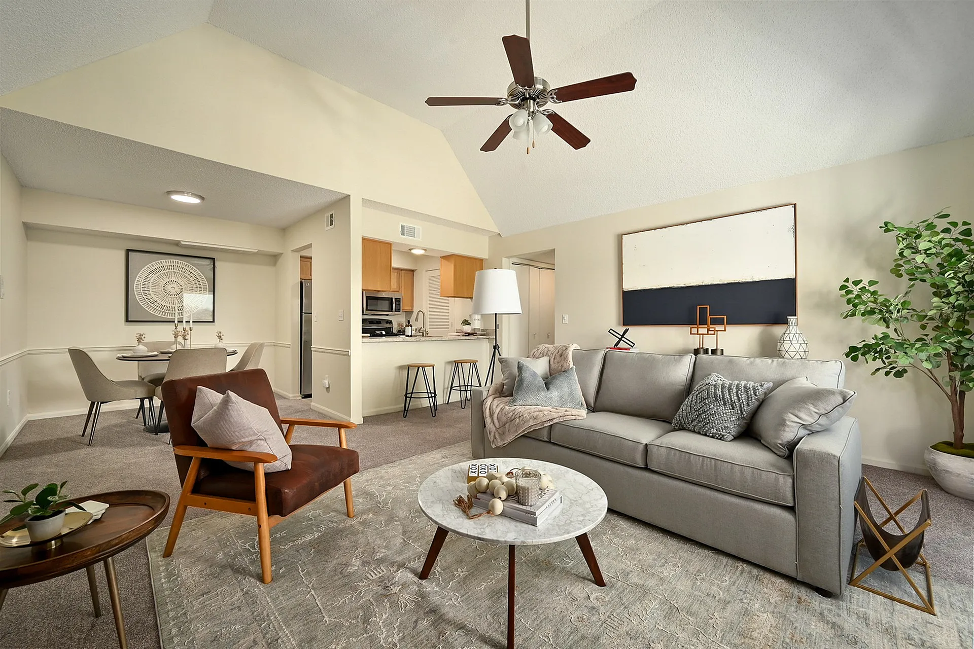 Chic and cozy open-plan living room with a plush gray sofa, modern armchair, stylish decor, and a breakfast bar opening to the kitchen.
