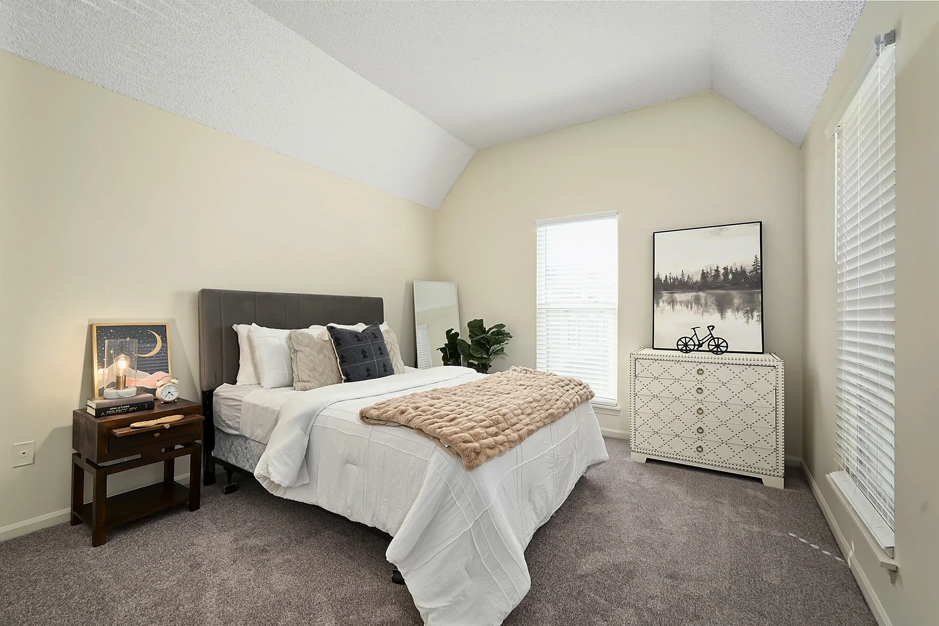 Cozy bedroom featuring a plush bed with elegant cushions, a stylish nightstand, and tasteful decor under vaulted ceilings with soft natural light.