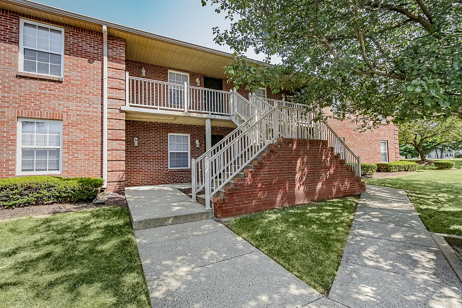 Charming brick apartment building with inviting outdoor staircase and lush green surroundings.
