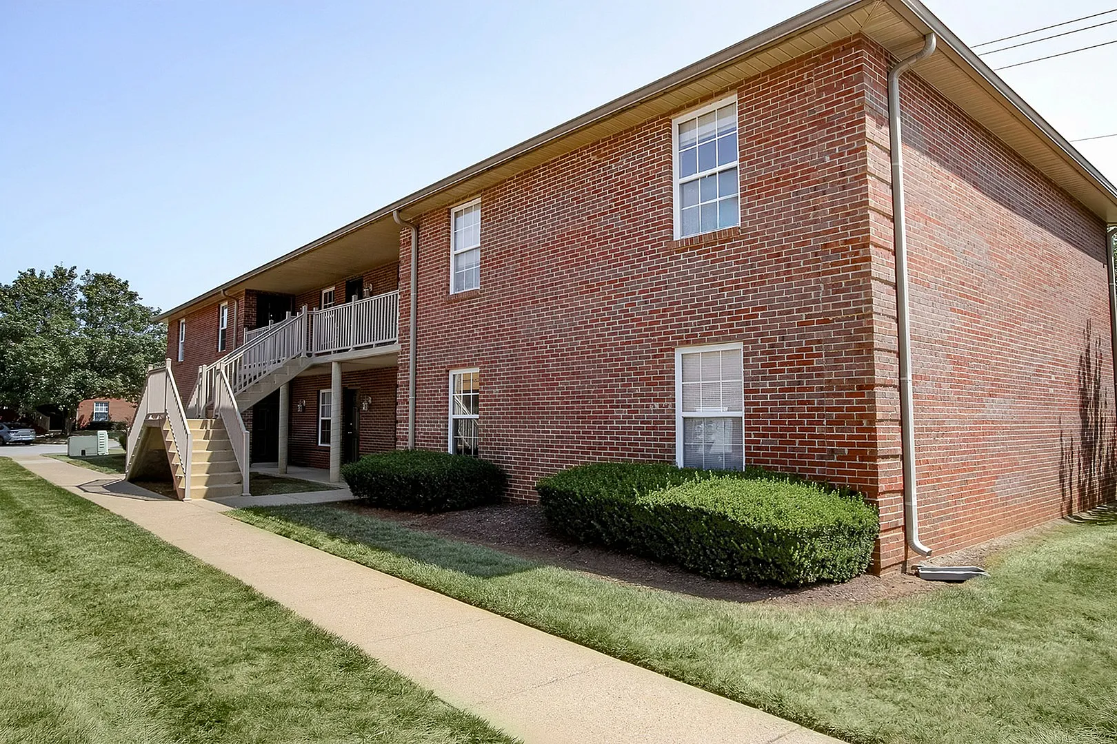 Charming red-brick apartment building with a well-maintained lawn, featuring accessible stairs and a cozy front entrance.