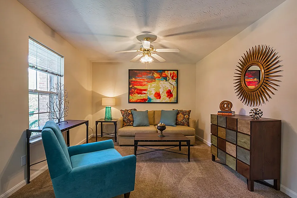 Charming living room featuring a cozy beige sofa, vibrant artwork, and a sunburst mirror, accented by an elegant teal chair and a modern side table.