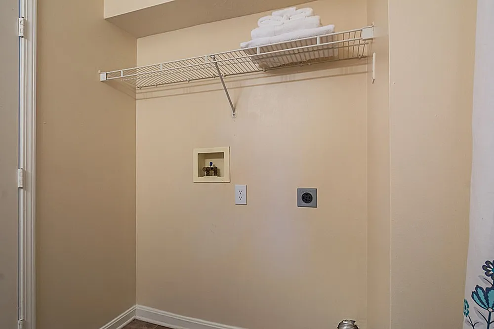Bright utility nook featuring wall-mounted shelving and laundry connections, ideal for maximizing space and organization.