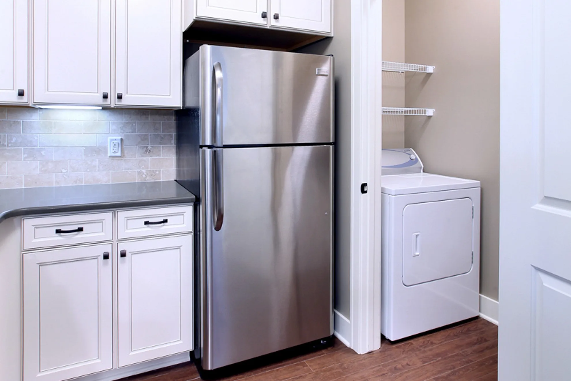 Modern kitchen with stainless steel refrigerator, elegant cabinetry, and convenient in-unit laundry.