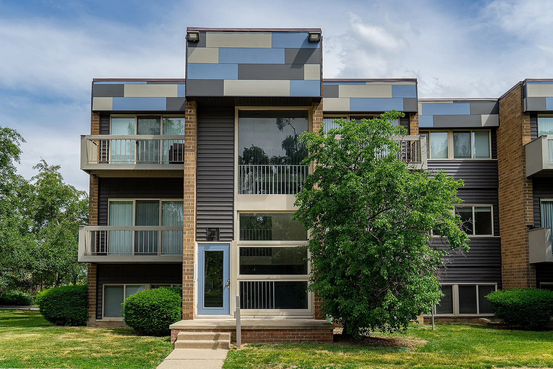 Modern apartment building with sleek design, large windows, and private balconies, surrounded by lush greenery.