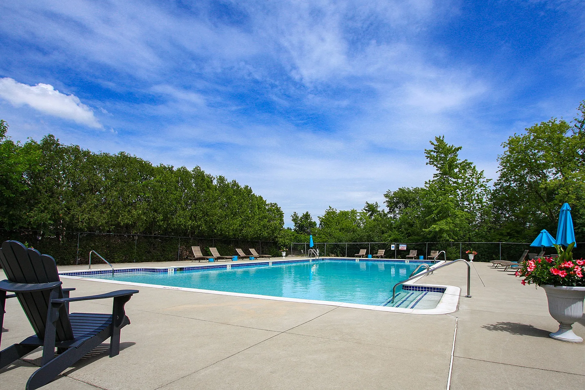 Relaxing outdoor pool area with lush greenery, lounge chairs, and blue skies, perfect for leisurely afternoons.