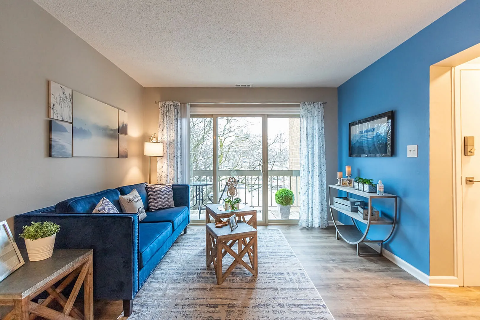 Modern living room with stylish blue accents, cozy seating, and bright natural light from large windows overlooking a serene view.