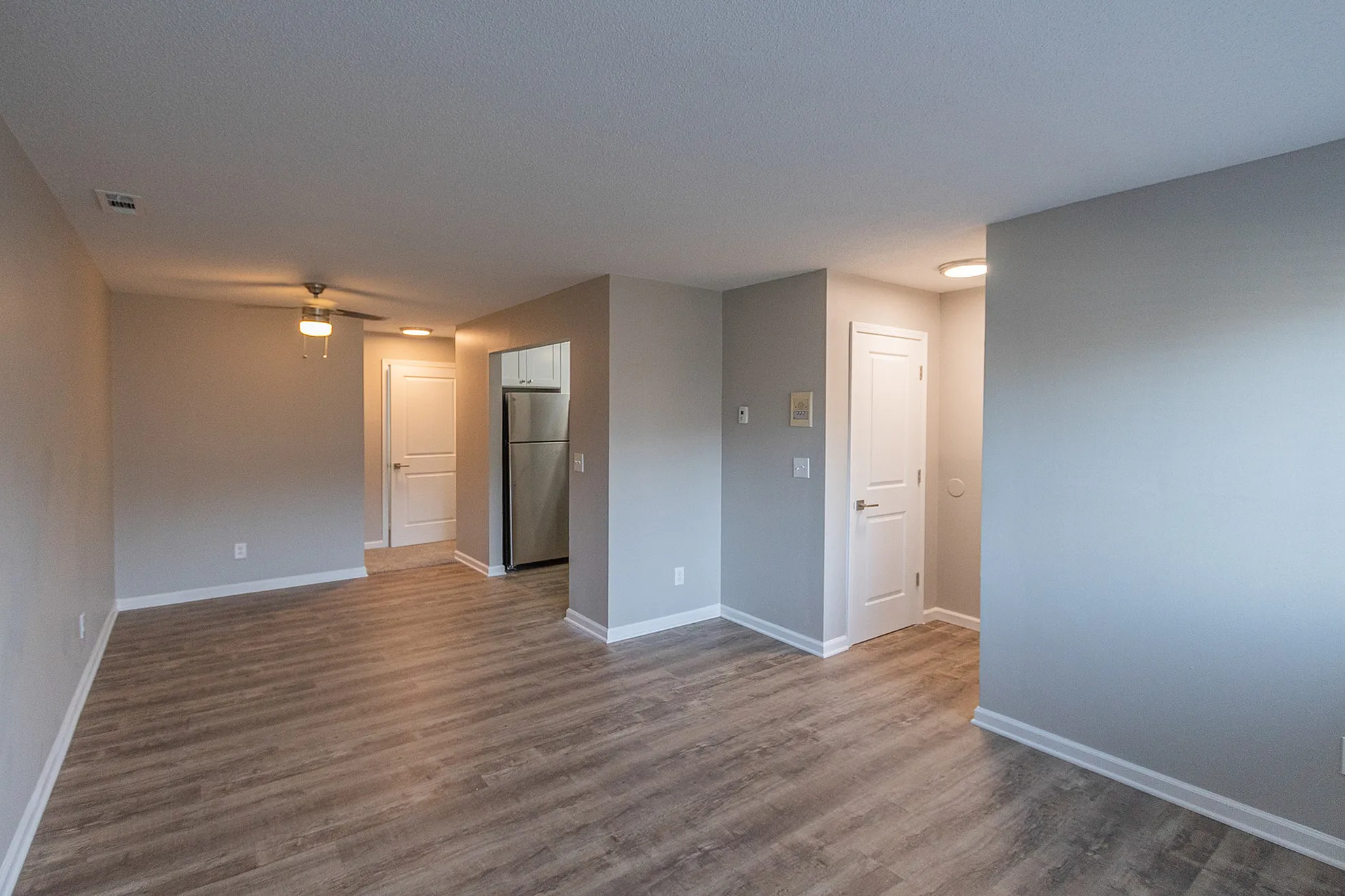 Modern apartment with sleek laminate flooring, featuring a spacious hallway leading to a contemporary kitchen with stainless steel appliances.