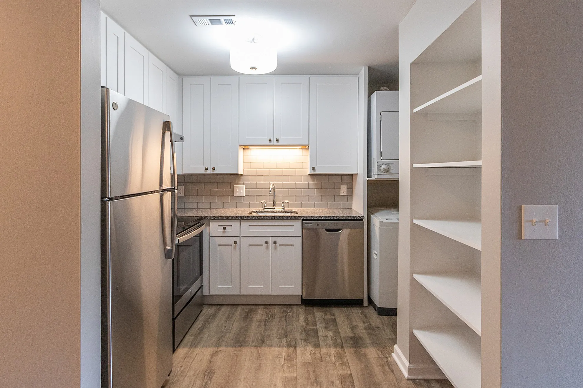 Modern kitchen with sleek stainless steel appliances, elegant white cabinetry, and stylish tile backsplash, featuring convenient in-unit laundry and open shelving.