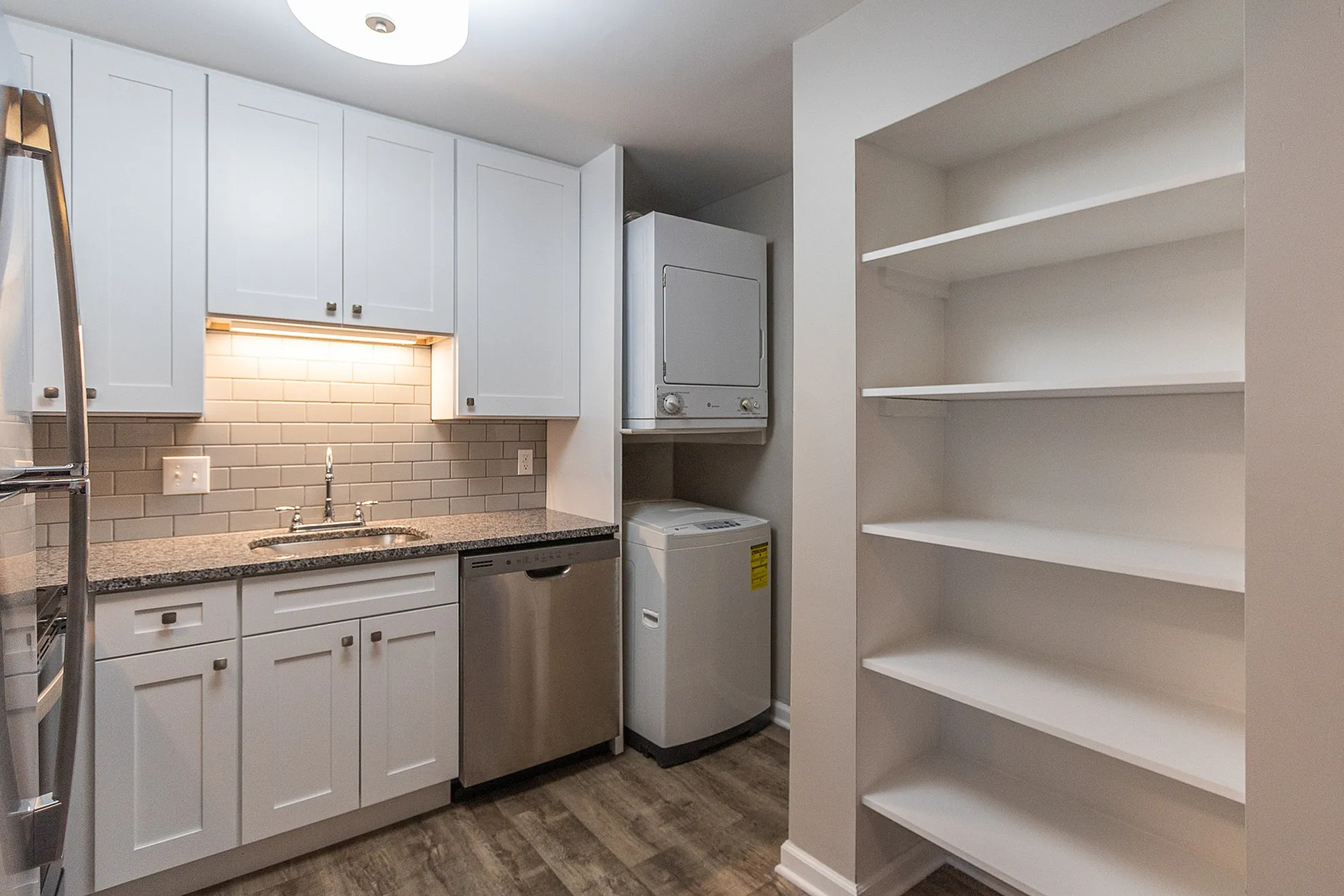 Modern kitchen with sleek granite countertops, stainless steel appliances, and integrated washer and dryer. Ample white cabinetry and built-in shelving for optimal organization.