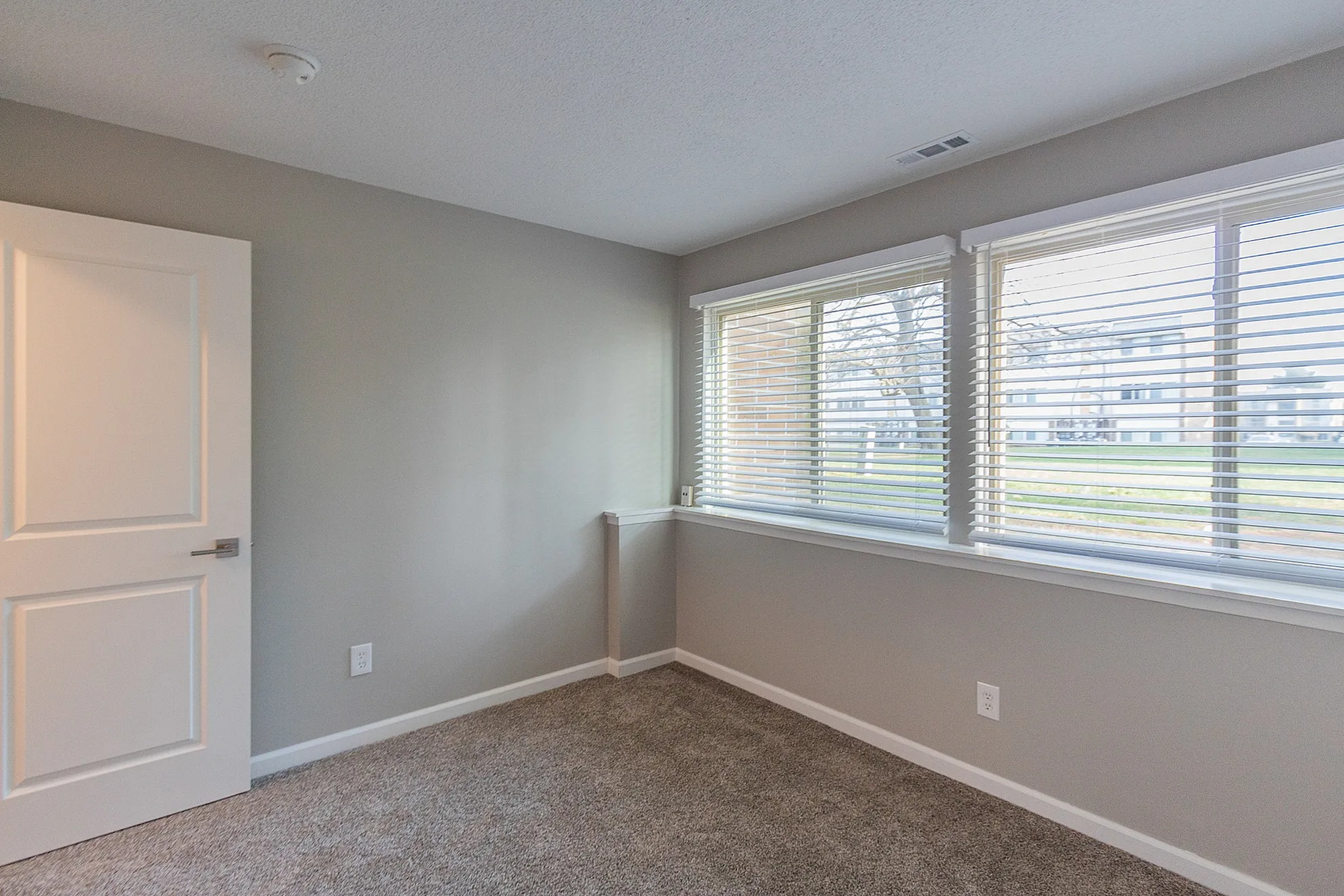 Bright and airy bedroom with large windows, modern carpeting, and fresh gray walls, offering a welcoming atmosphere.