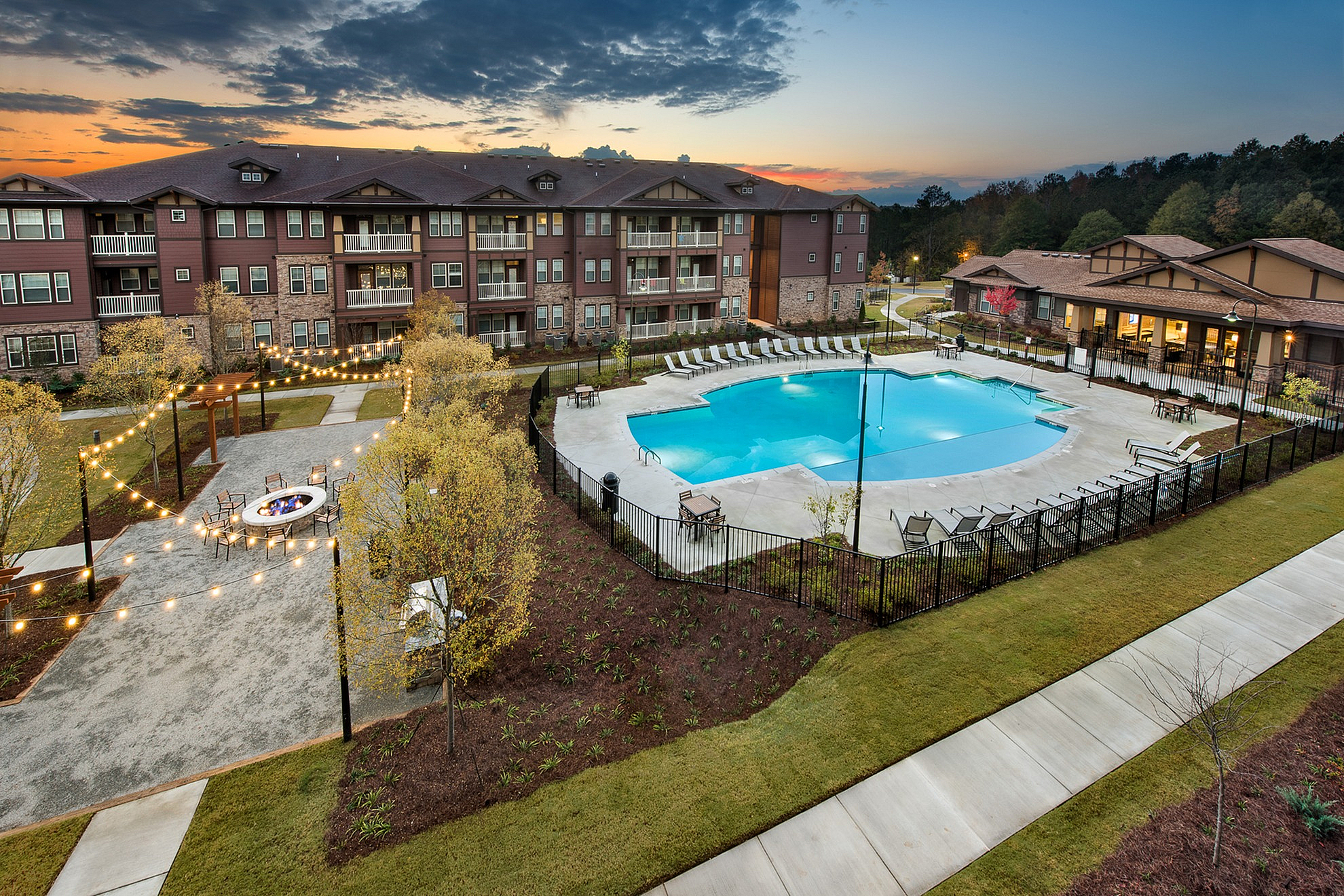Luxurious apartment complex with a tranquil swimming pool and inviting outdoor lounge area, set against a stunning sunset backdrop.