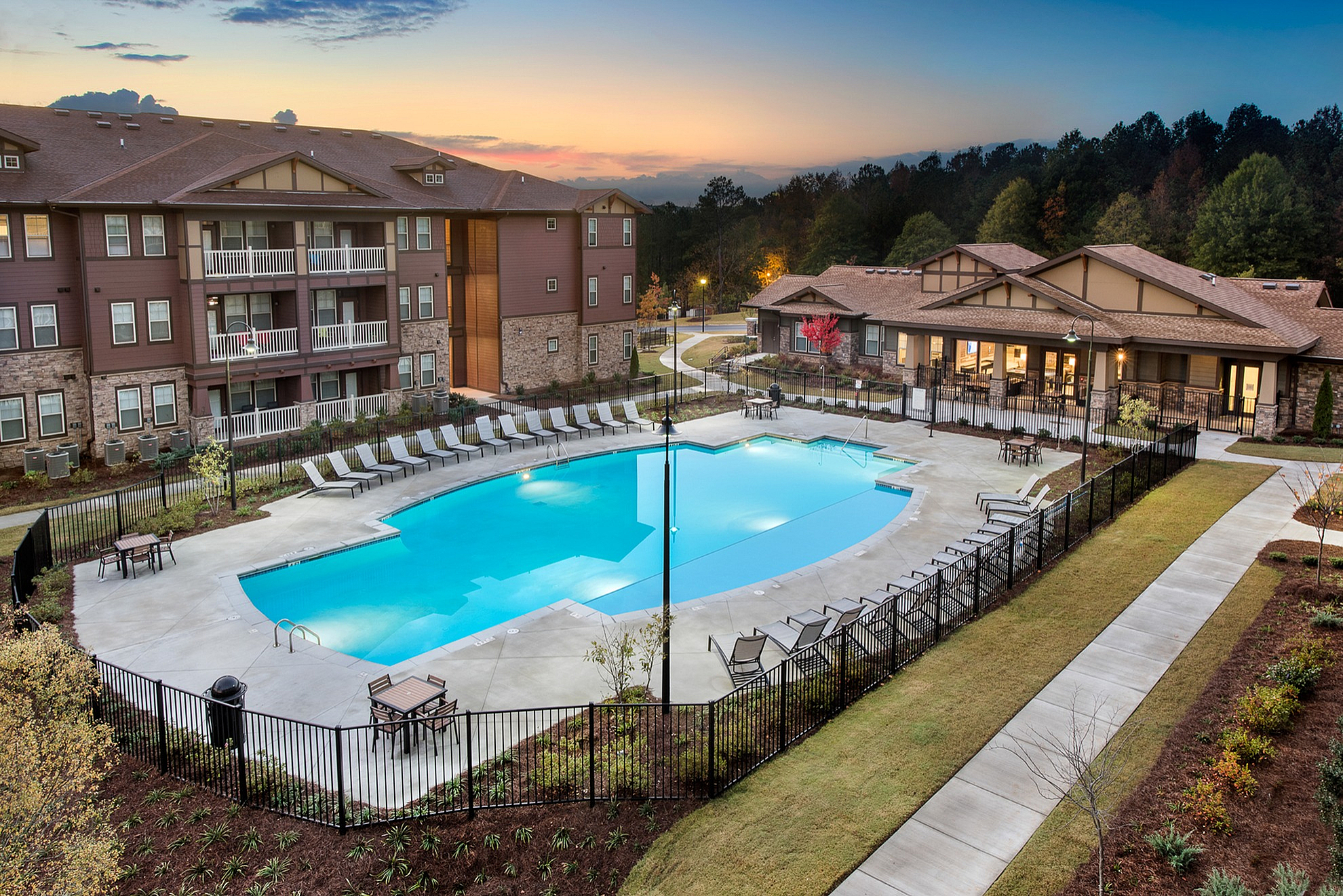 Beautiful apartment complex at sunset with inviting pool, lounge chairs, and landscaped pathways creating a serene living environment.