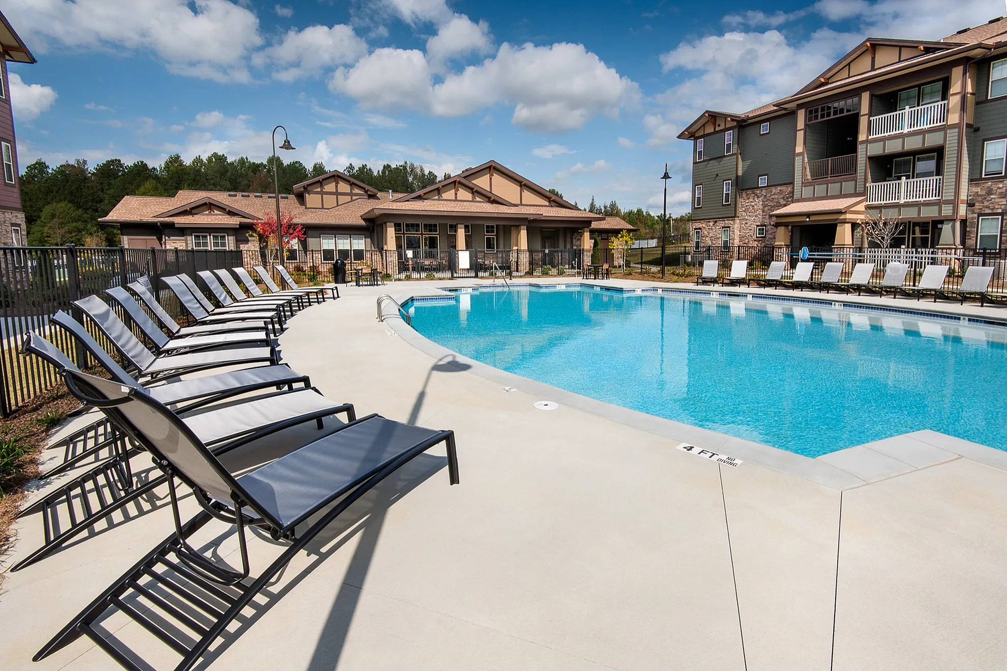 Inviting outdoor pool area with modern loungers, surrounded by stylish apartment buildings under a bright blue sky.