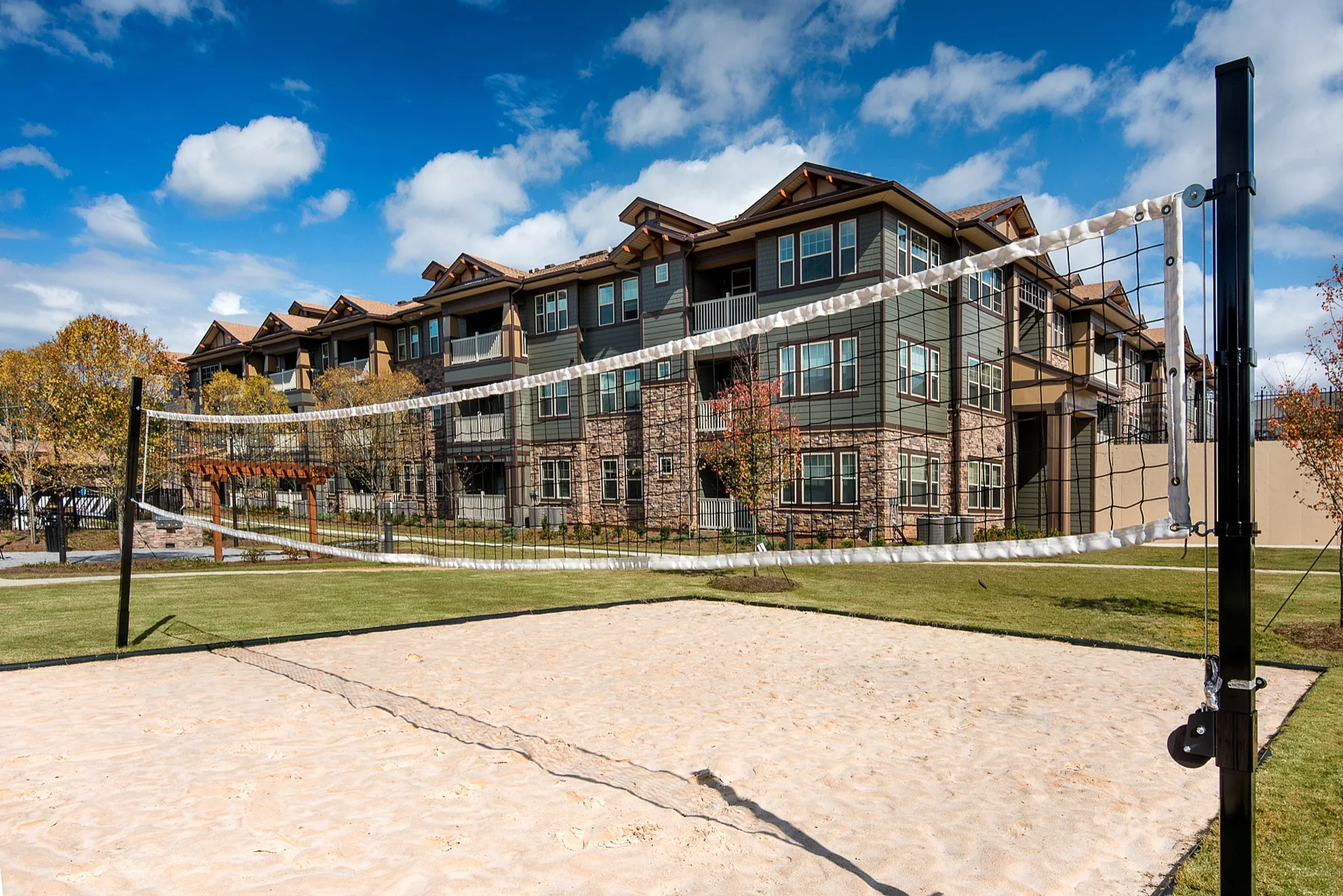Modern apartment complex with sand volleyball court, manicured lawns, and elegant stone facade.