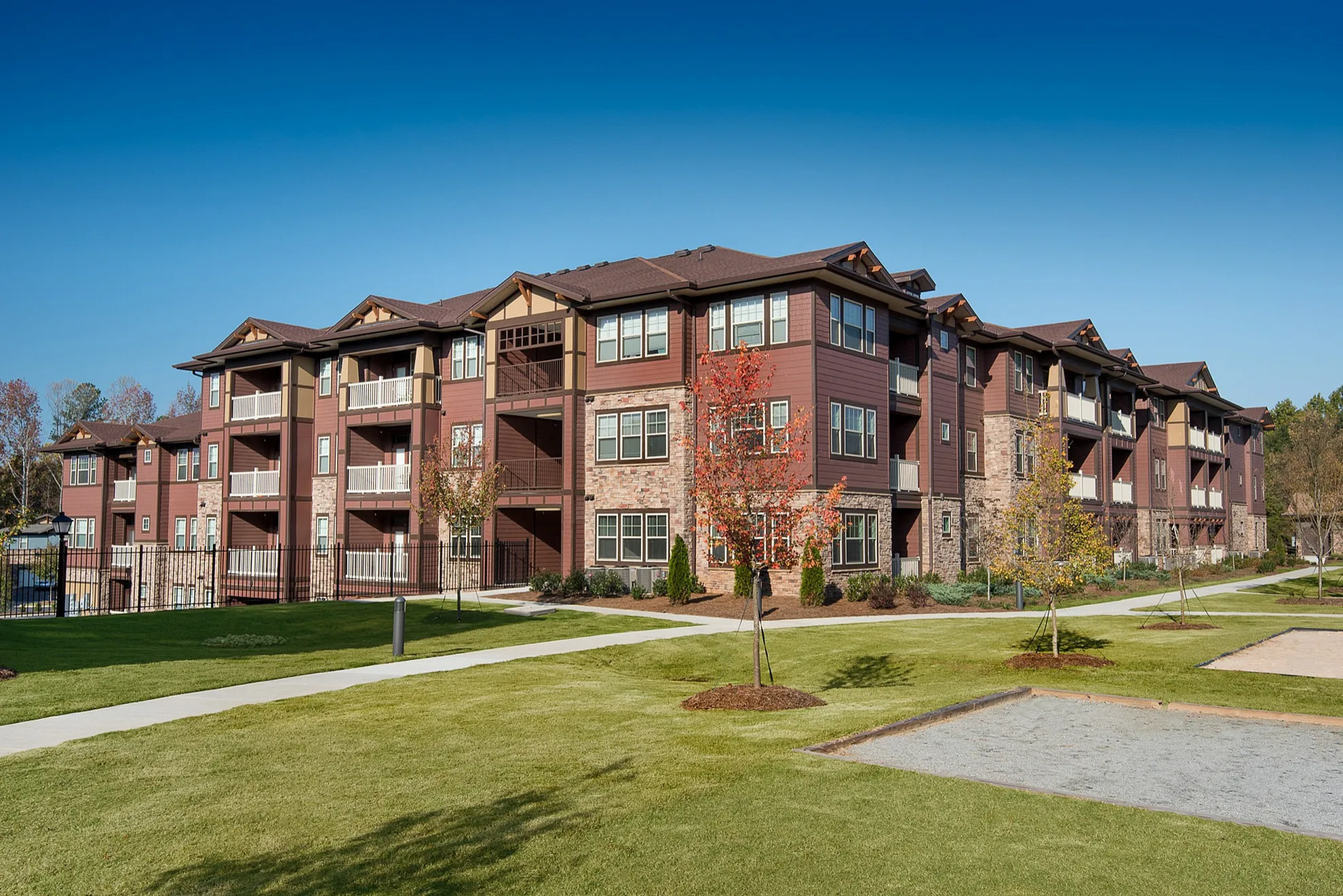 Charming apartment building with modern architecture, featuring balconies and surrounded by lush green lawns and a blue sky backdrop.
