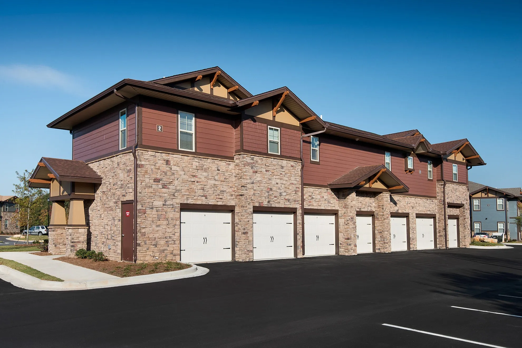 Charming two-story apartment building with elegant stone facade and multiple garages, nestled in a picturesque neighborhood.