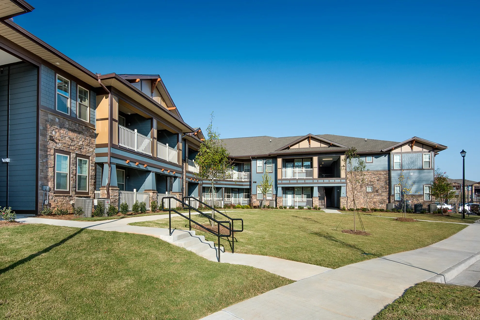 Charming apartment complex with modern architecture, lush green lawns, and inviting walkways under a bright blue sky.