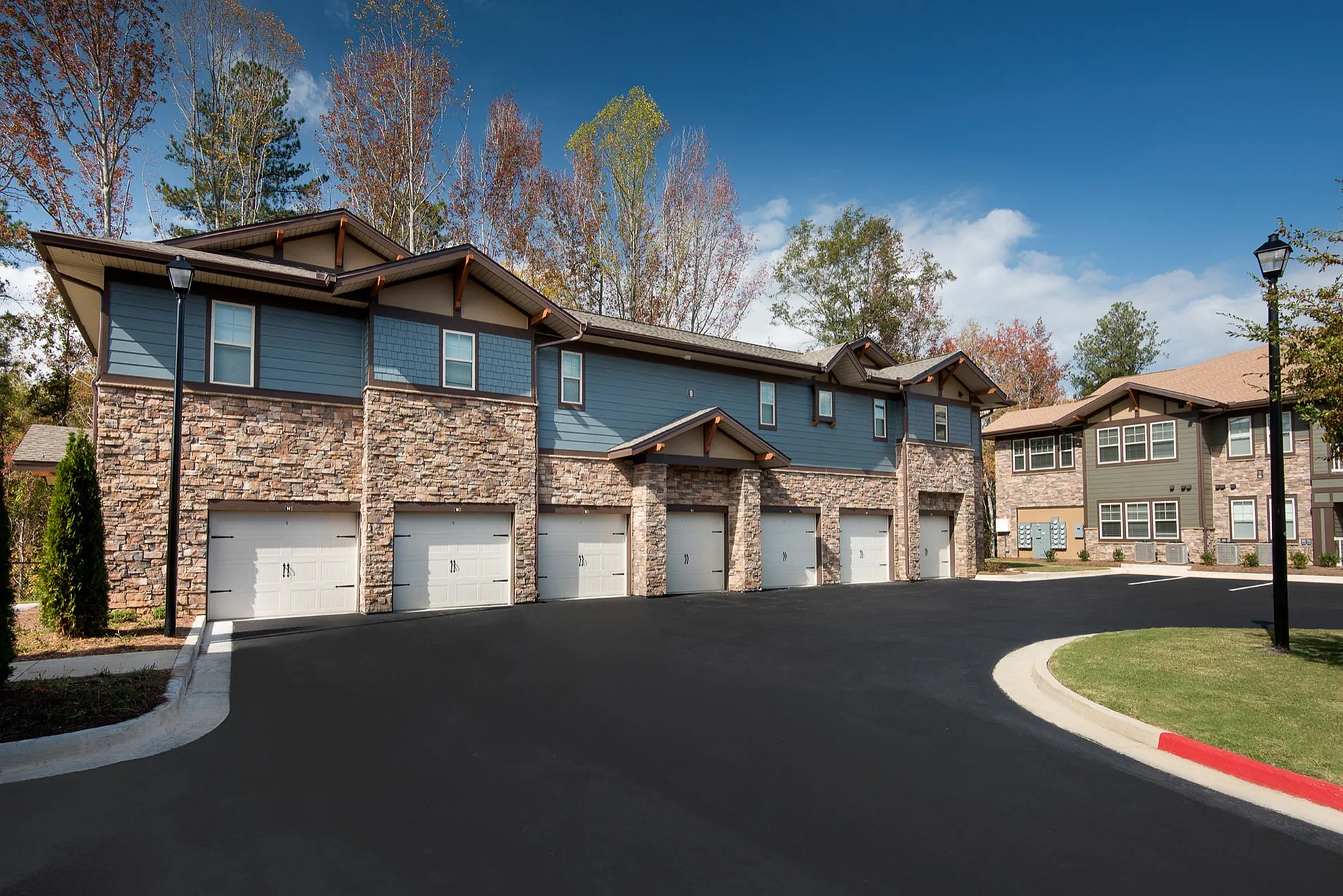 Charming modern townhouse complex with stone facades and attached garages, surrounded by lush greenery and vibrant sky.