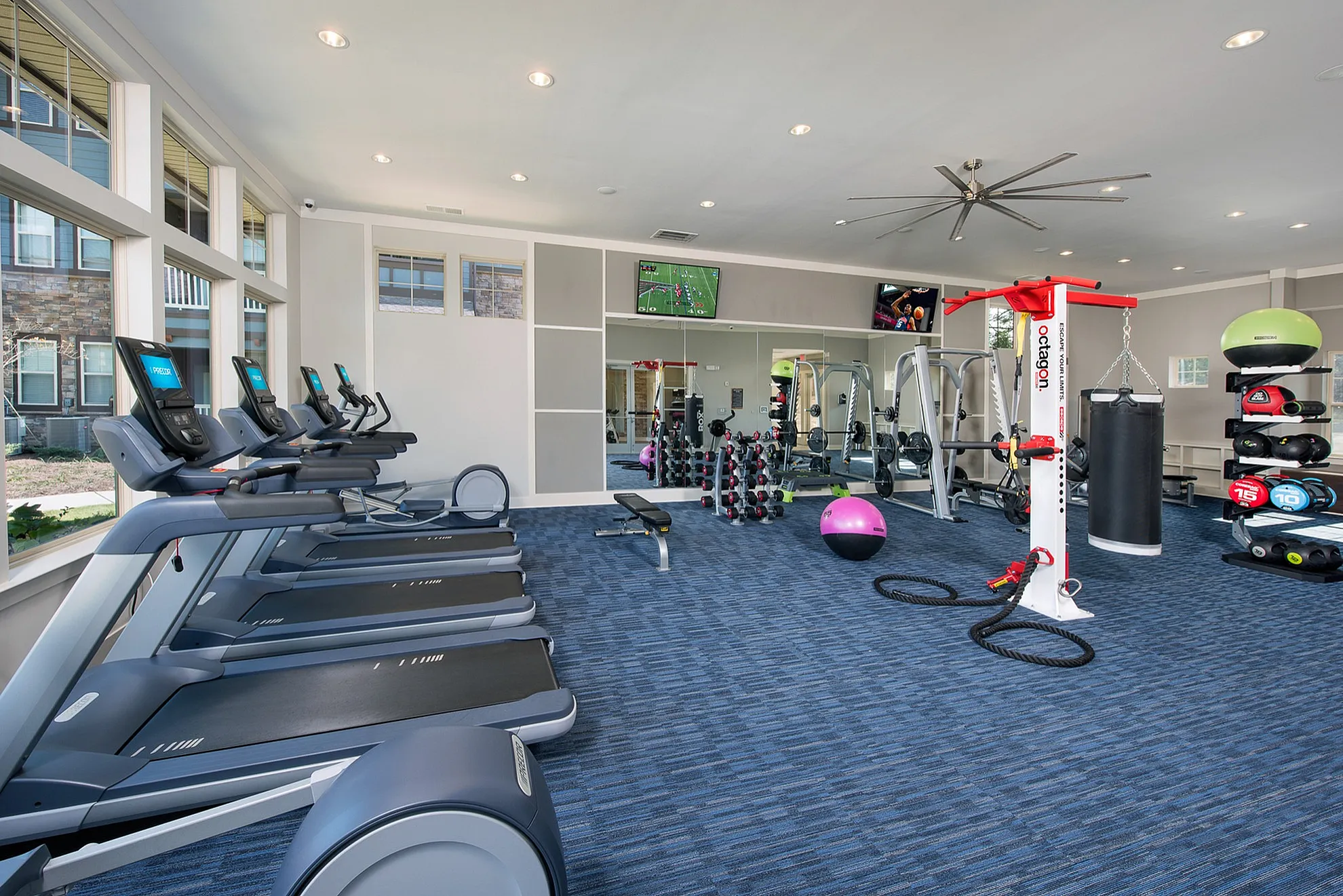 Contemporary fitness center with treadmills, weight equipment, punching bag, and bright spacious interior.