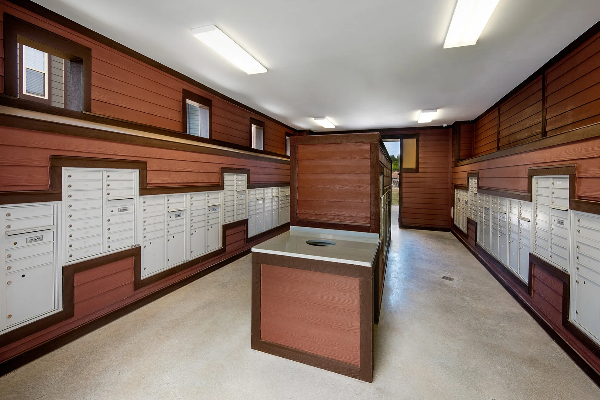 Modern apartment mailroom with rustic wooden paneling and ample secured mailboxes.
