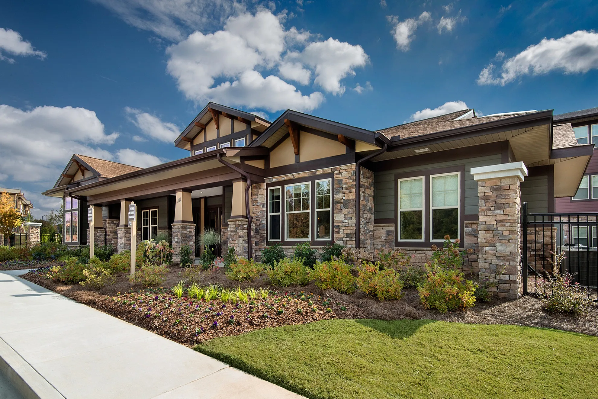 Charming suburban home with stone facade, manicured lawn, and vibrant garden under a clear blue sky.
