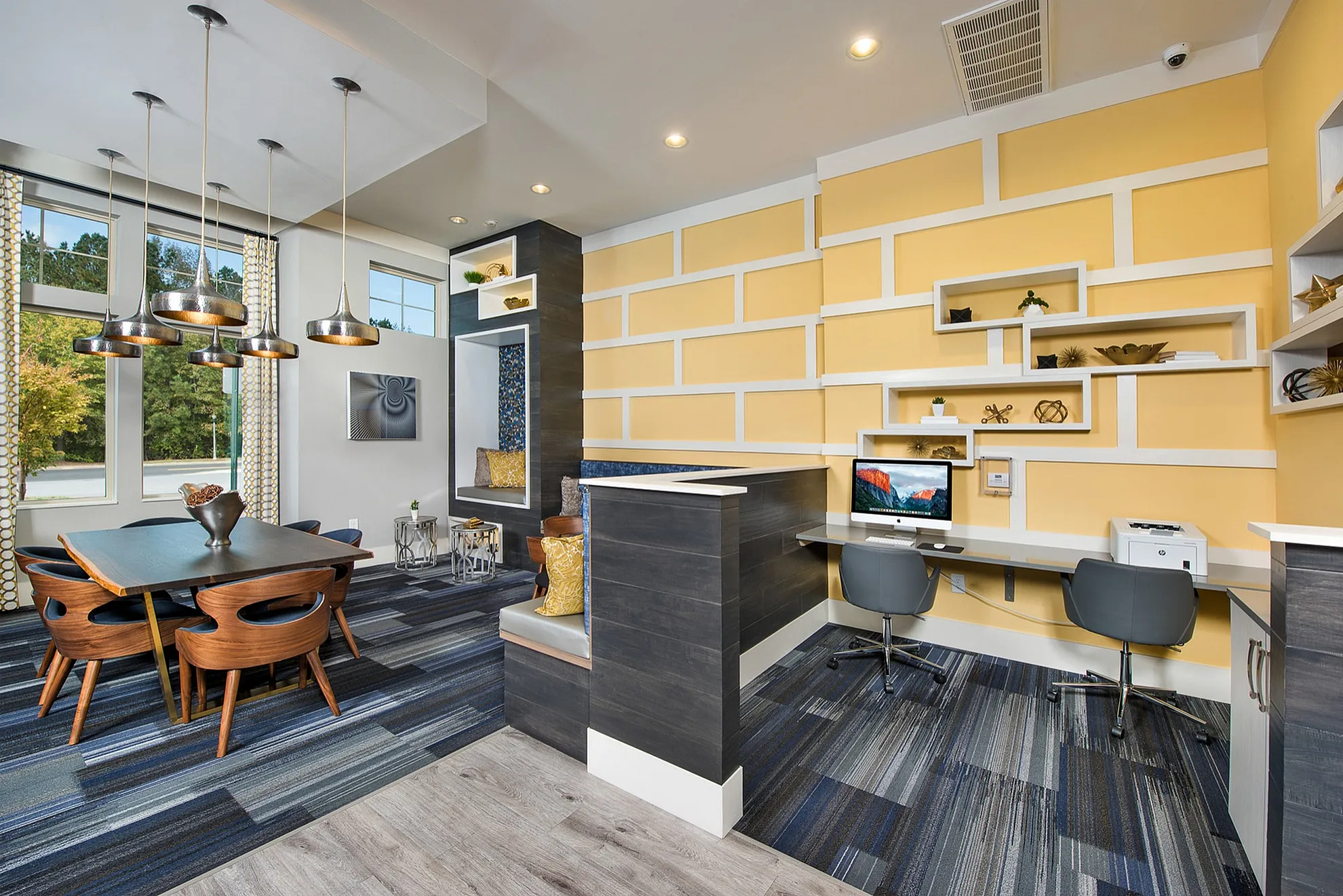 Modern co-working space with vibrant yellow walls, stylish pendant lights, and a chic wooden table overlooking large windows with scenic views.