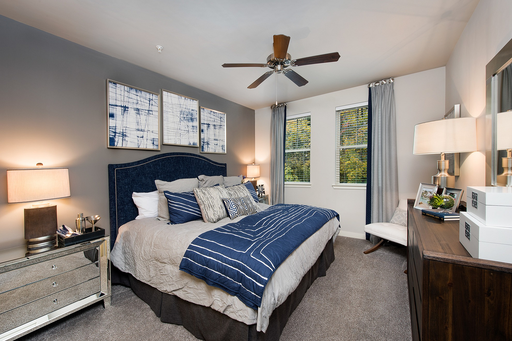 Elegant bedroom featuring a plush bed with blue accents, stylish modern decor, and ample natural light through large windows.