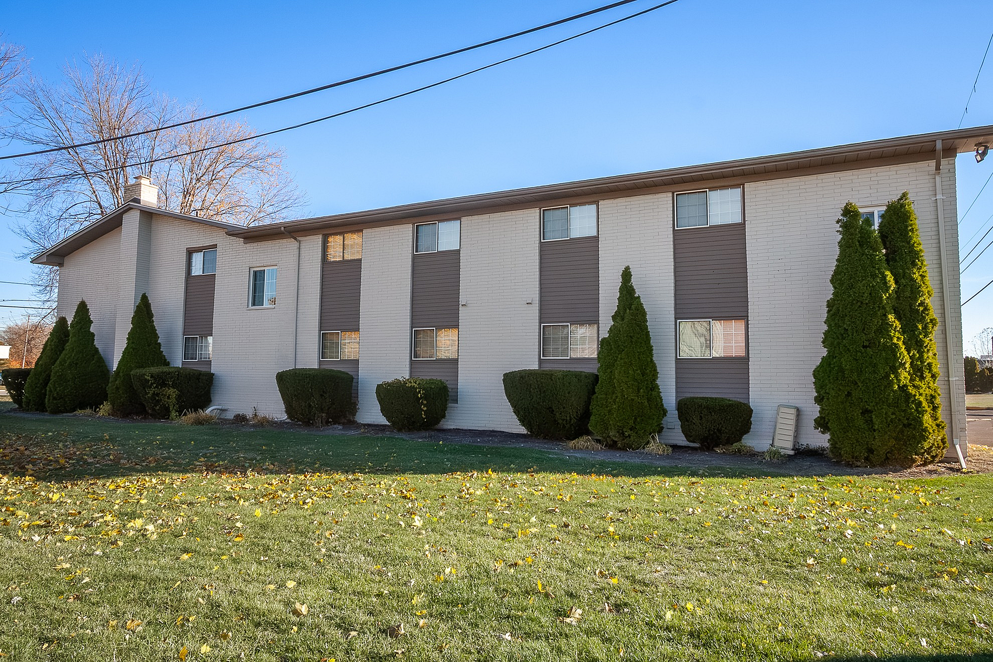 Charming apartment building with neatly trimmed hedges and spacious green area, offering a cozy suburban living experience.