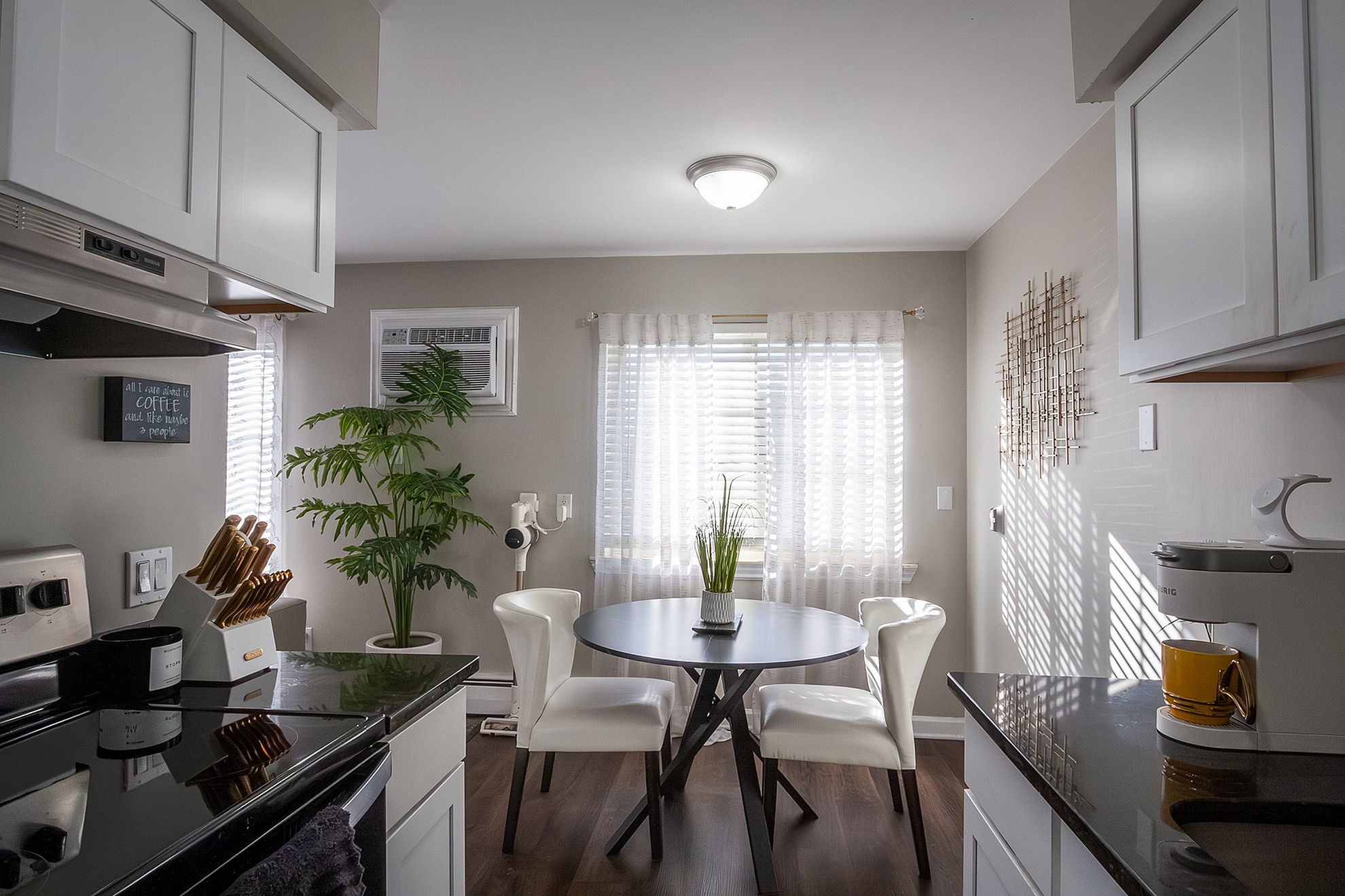 Charming kitchen with elegant white cabinetry, modern appliances, and a cozy dining nook illuminated by natural sunlight.