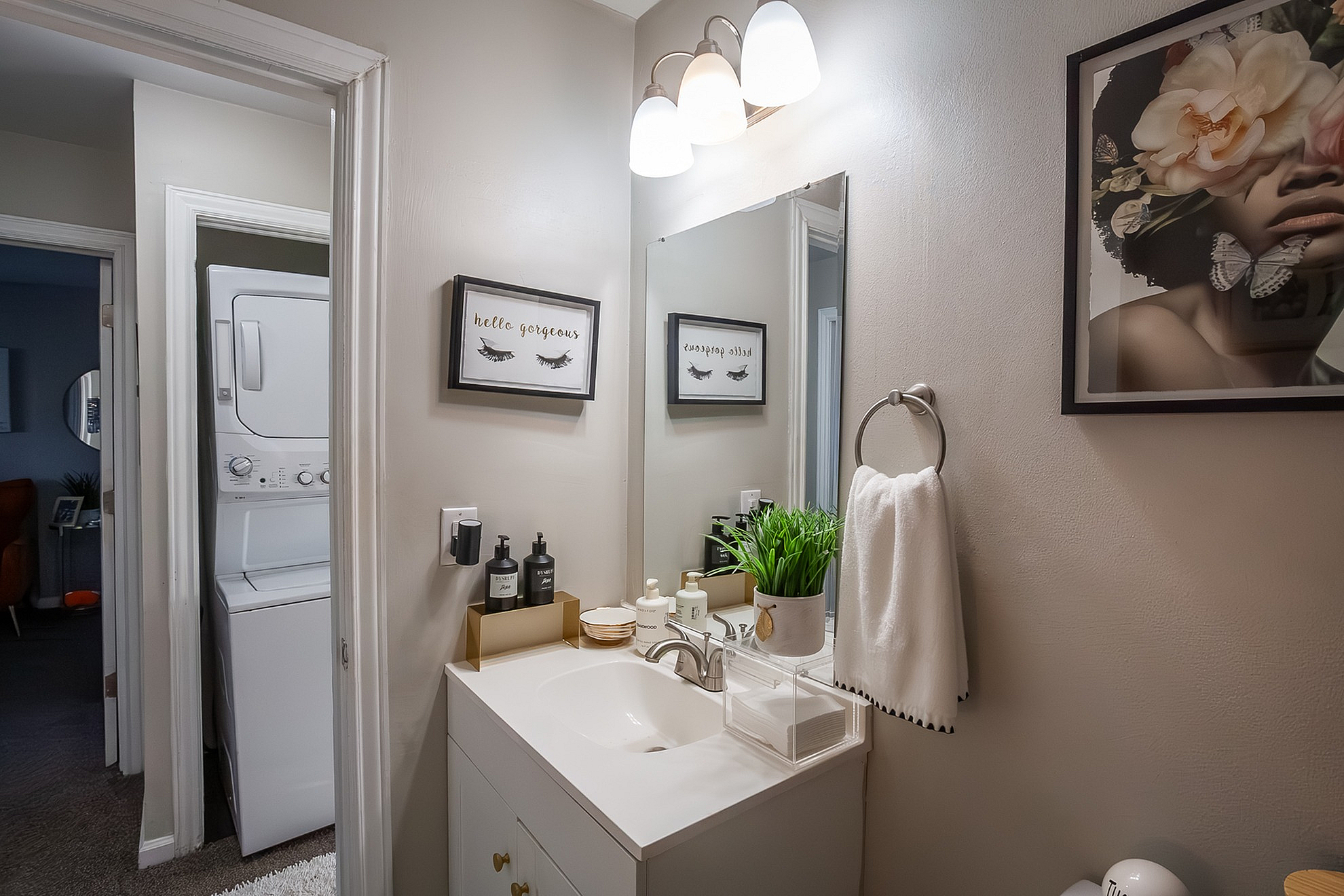 Chic bathroom showcasing elegant vanity, wall art, and convenient in-unit laundry setup.