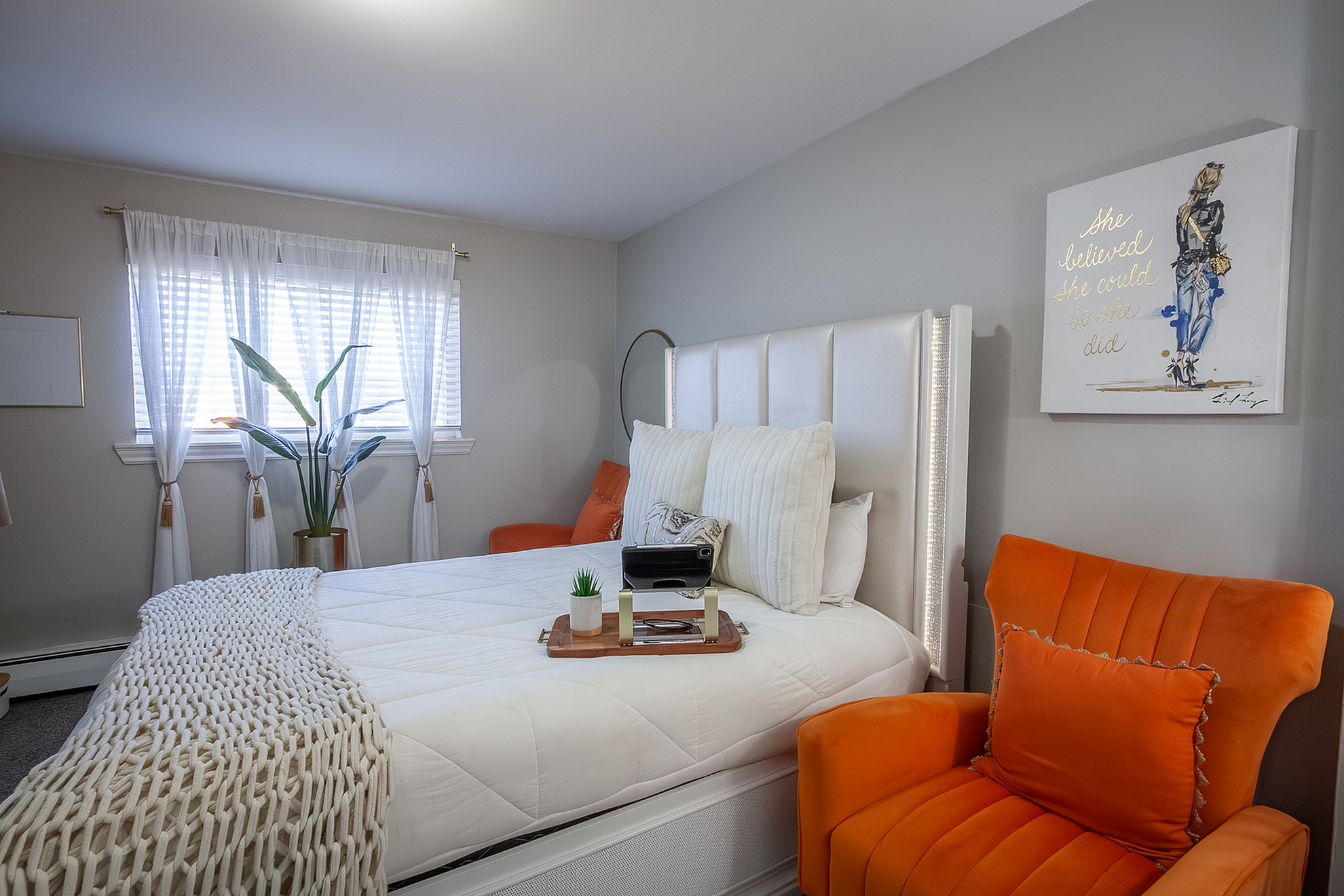 Chic bedroom showcasing a cozy bed with elegant white linens, vibrant orange armchairs, and stylish decor creating a welcoming atmosphere.