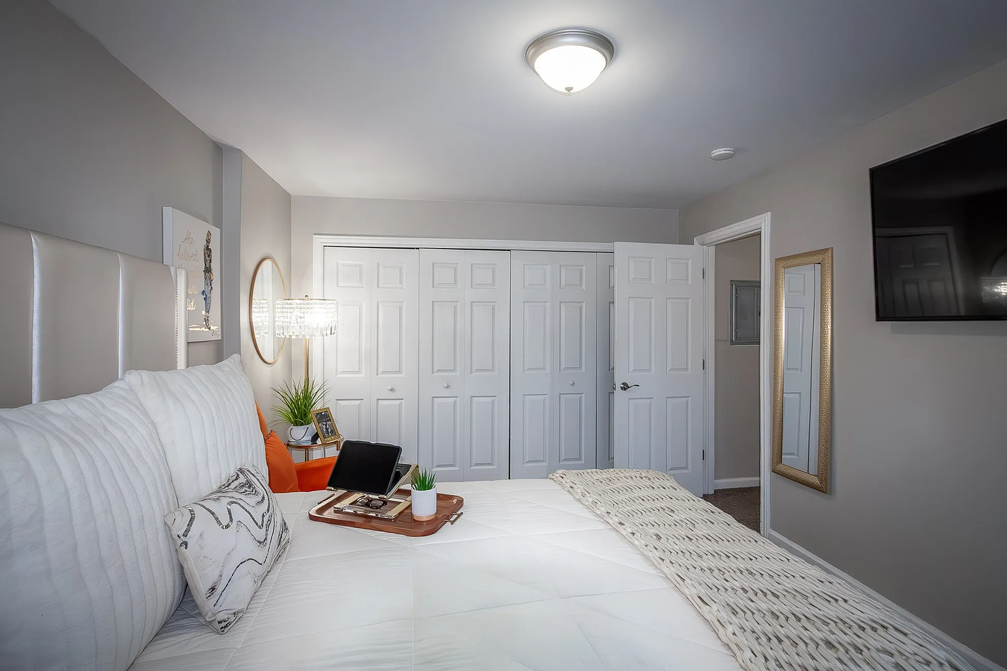 Elegant and cozy bedroom featuring a plush bed with accent pillows, stylish wall art, mirrored closet doors, and a modern chandelier.