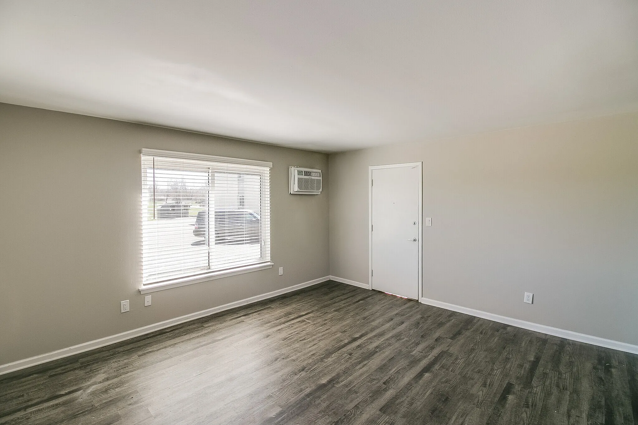Bright and airy living space with large window, modern gray flooring, and fresh white walls.