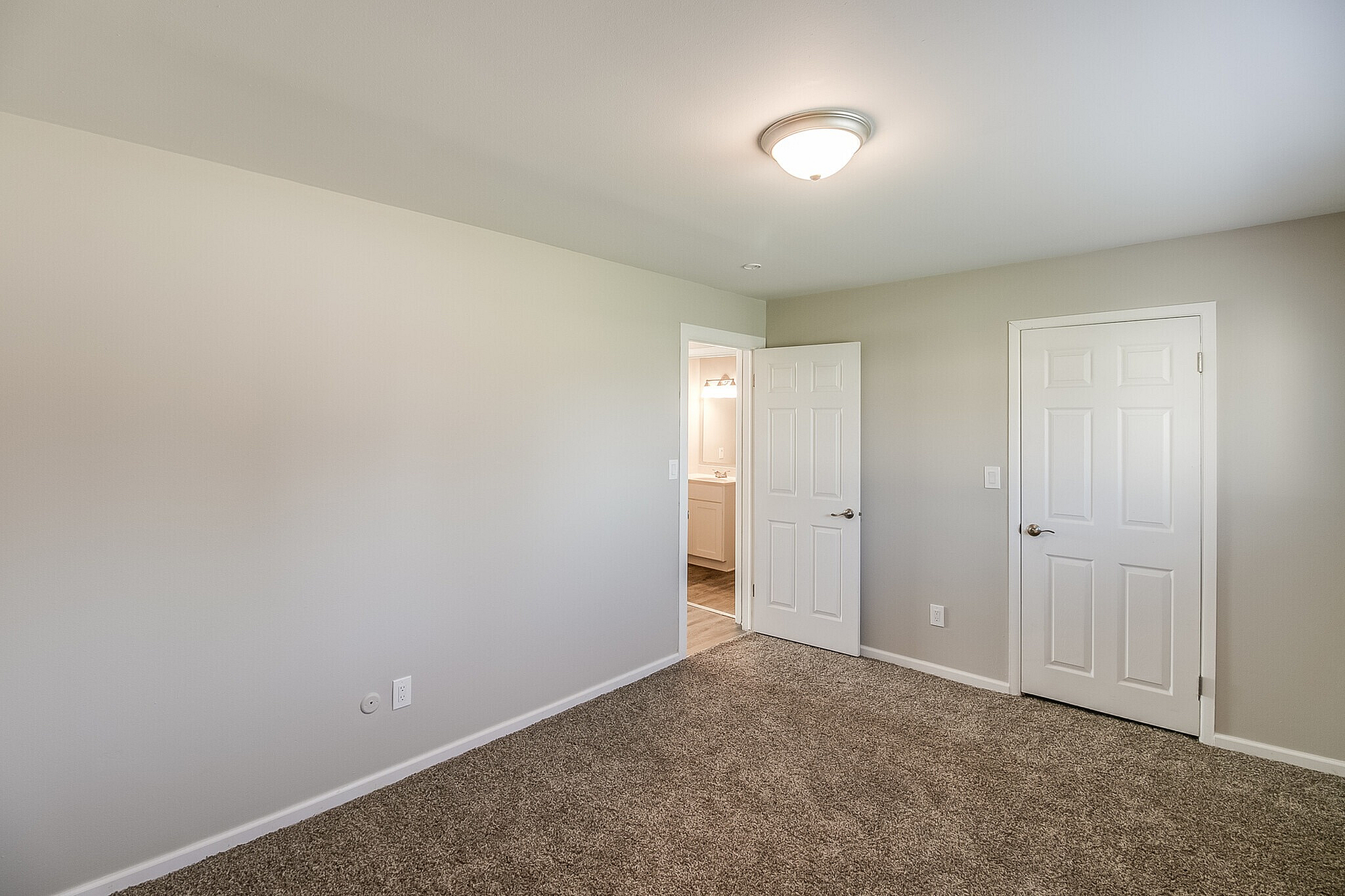 Bright, spacious bedroom featuring plush carpeting, neutral tones, and ample natural light with an en-suite bathroom in view.